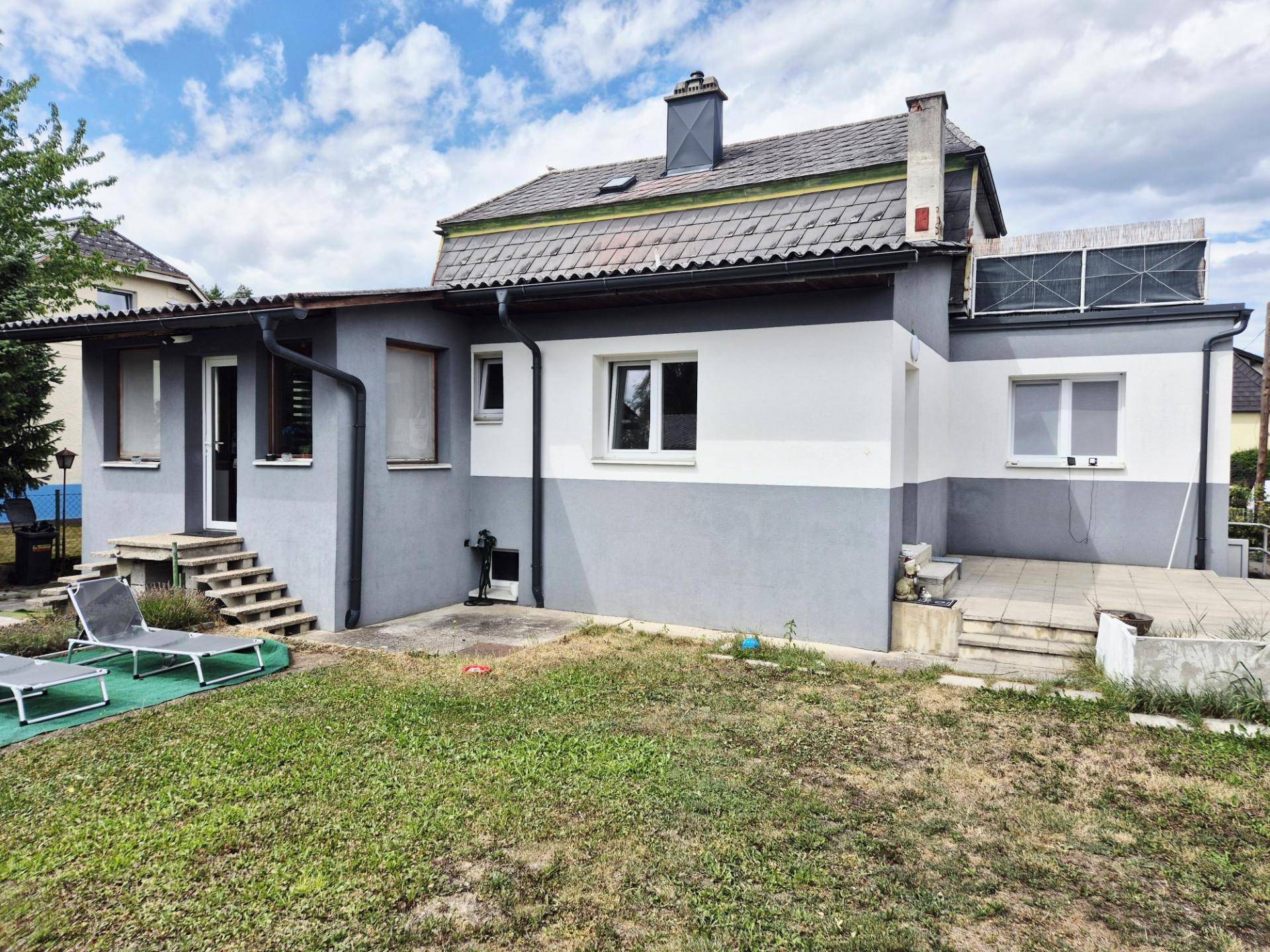 Rückansicht des Hauses mit großem Garten und Terrasse unter blauem Himmel.