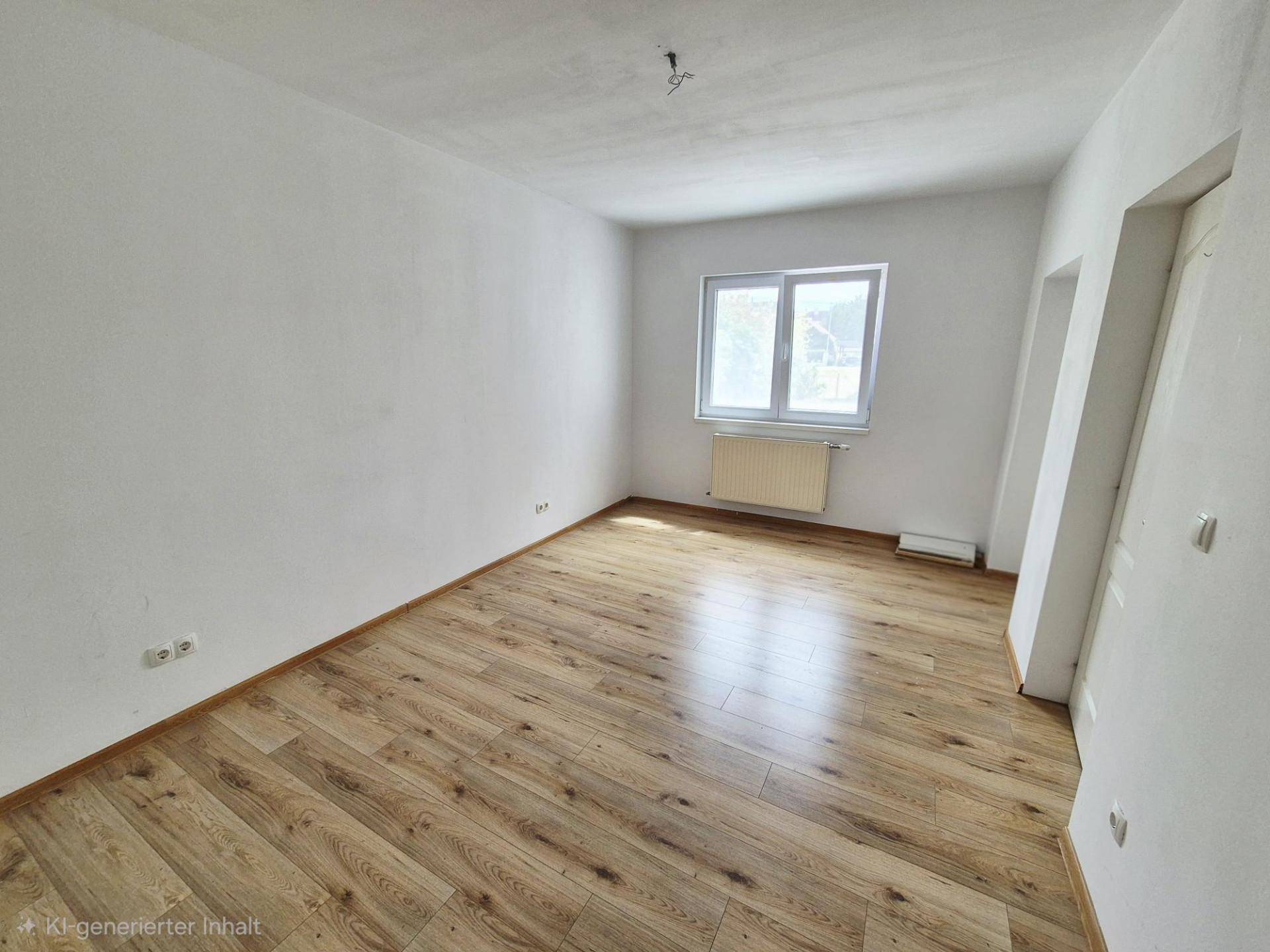 Helles Zimmer mit Laminatboden, weiß gestrichenen Wänden und Fenster.