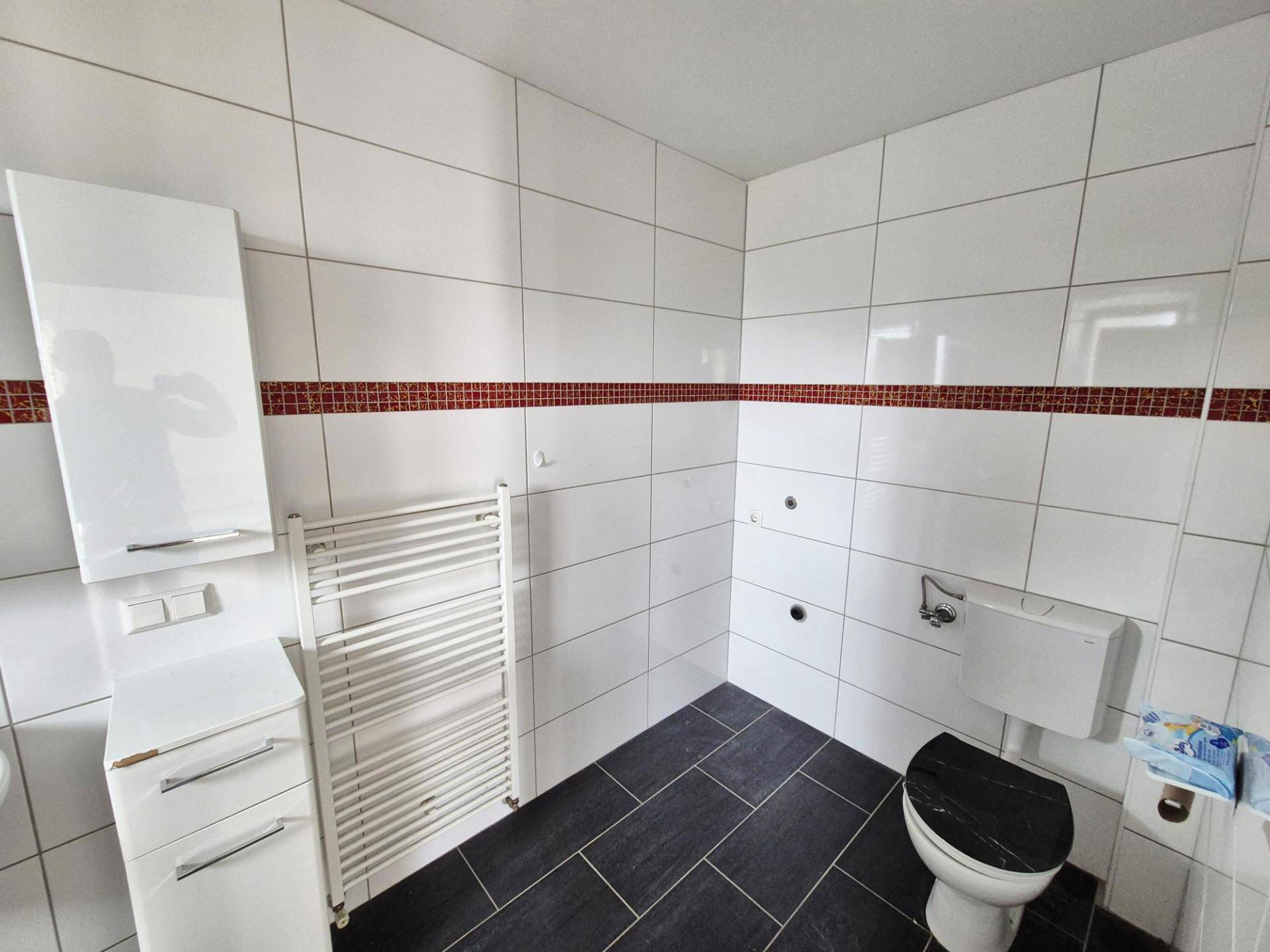 Modern gefliestes Badezimmer mit dunklem Boden und weißer Wandfliese, noch unvollendet.