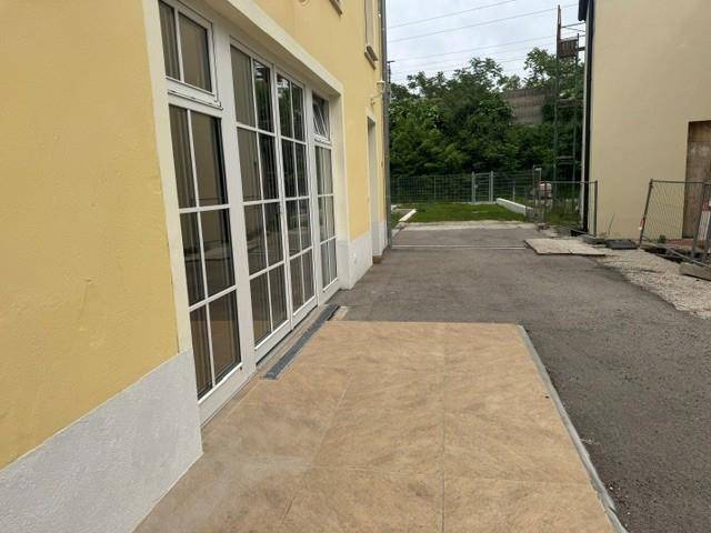 Außenansicht des Gebäudes mit einer kleinen gefliesten Terrasse und großen Fenstern.