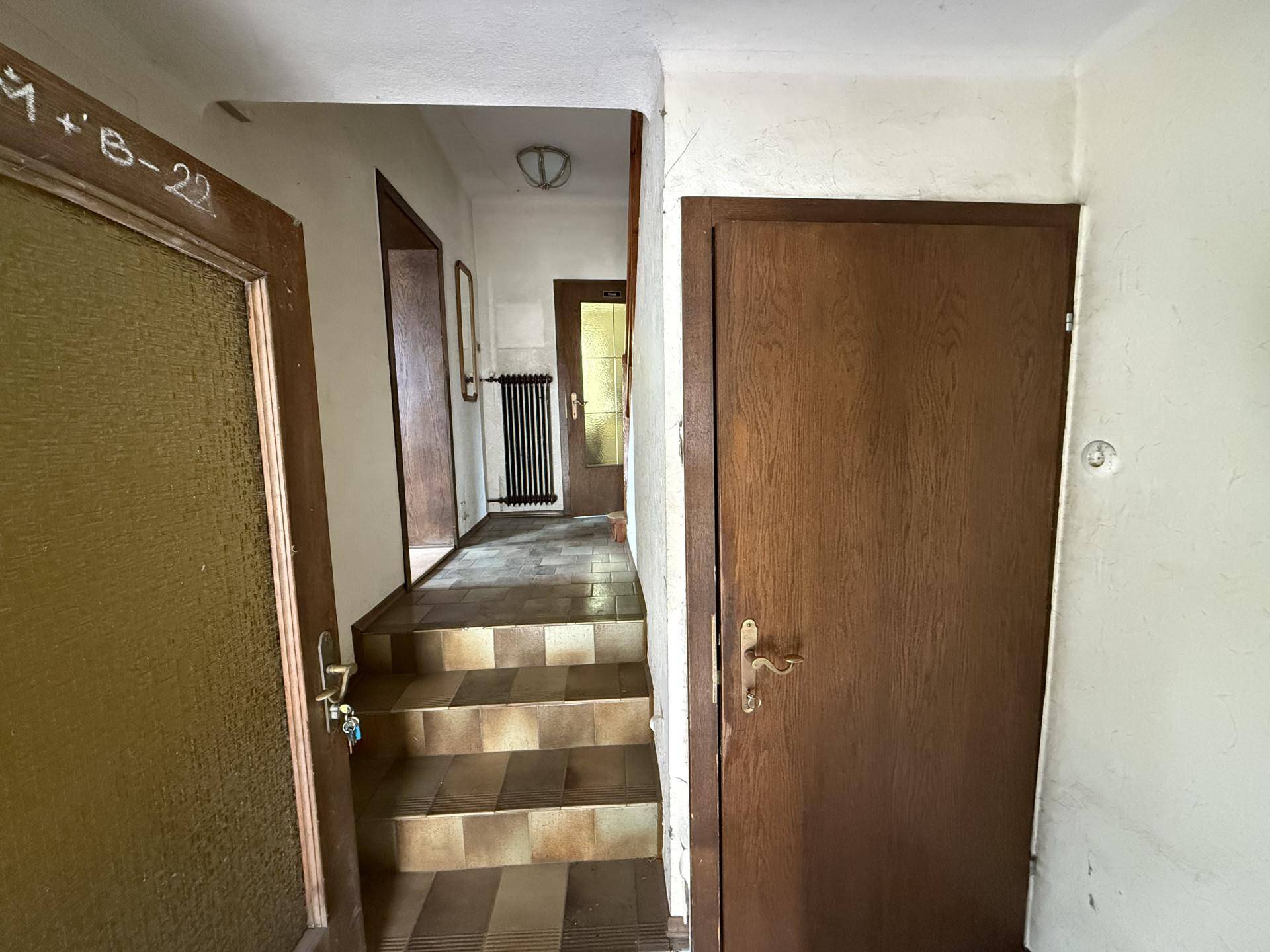 Ein Flur mit Holztreppe und gefliestem Boden, der zu weiteren Räumen im Haus führt.