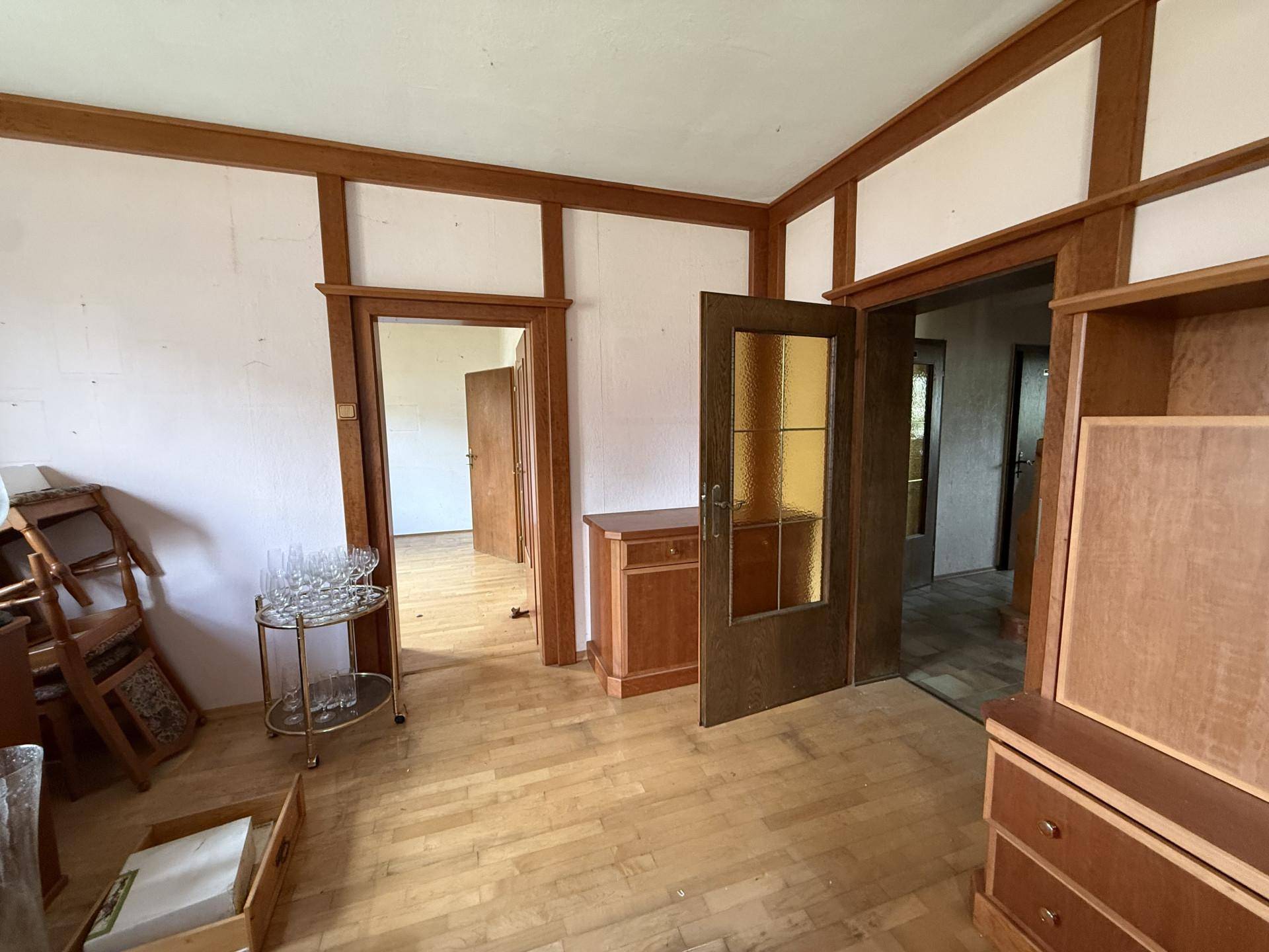 Ein Wohnzimmer mit Holzboden und mehreren Holztüren, die zu angrenzenden Räumen führen.
