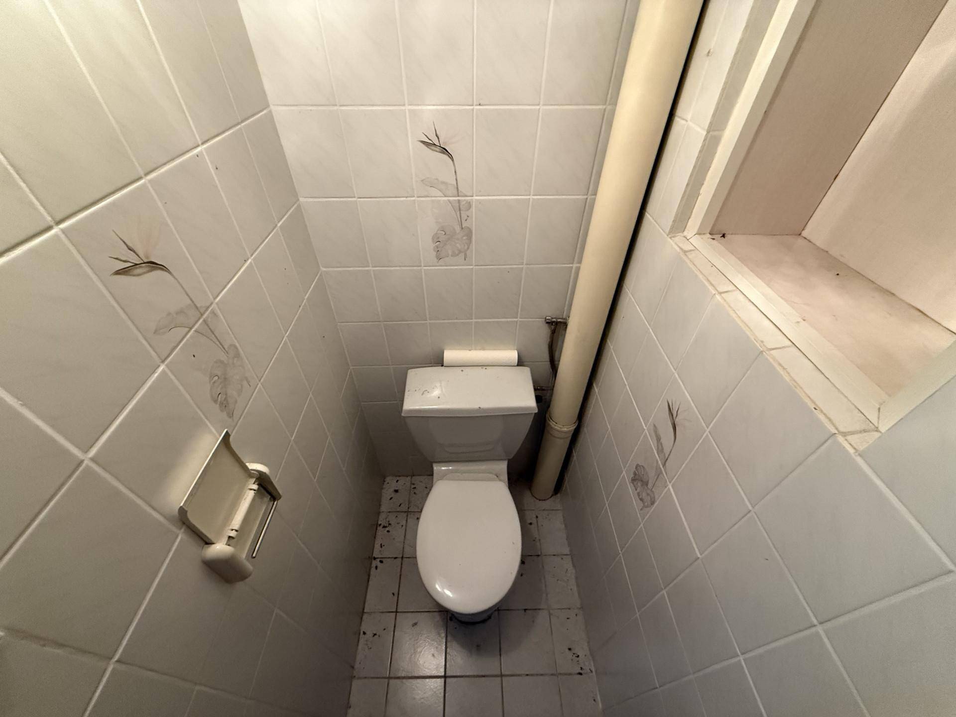 Eine kleine Toilette mit weißen Fliesen und einem Fenster, das für natürliche Belüftung sorgt.