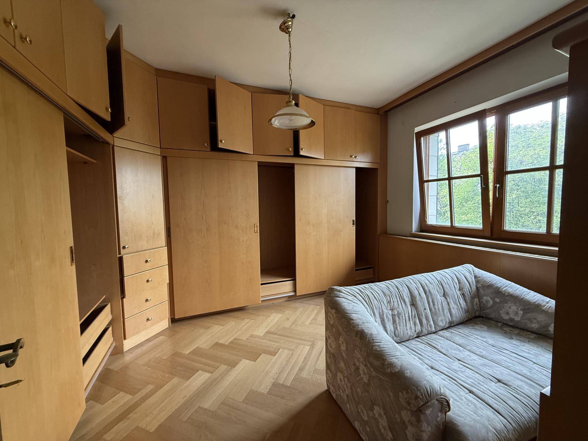 Ein Schlafzimmer mit umfangreichen Einbauschränken aus Holz und einem Sofa auf Fischgrätparkett.