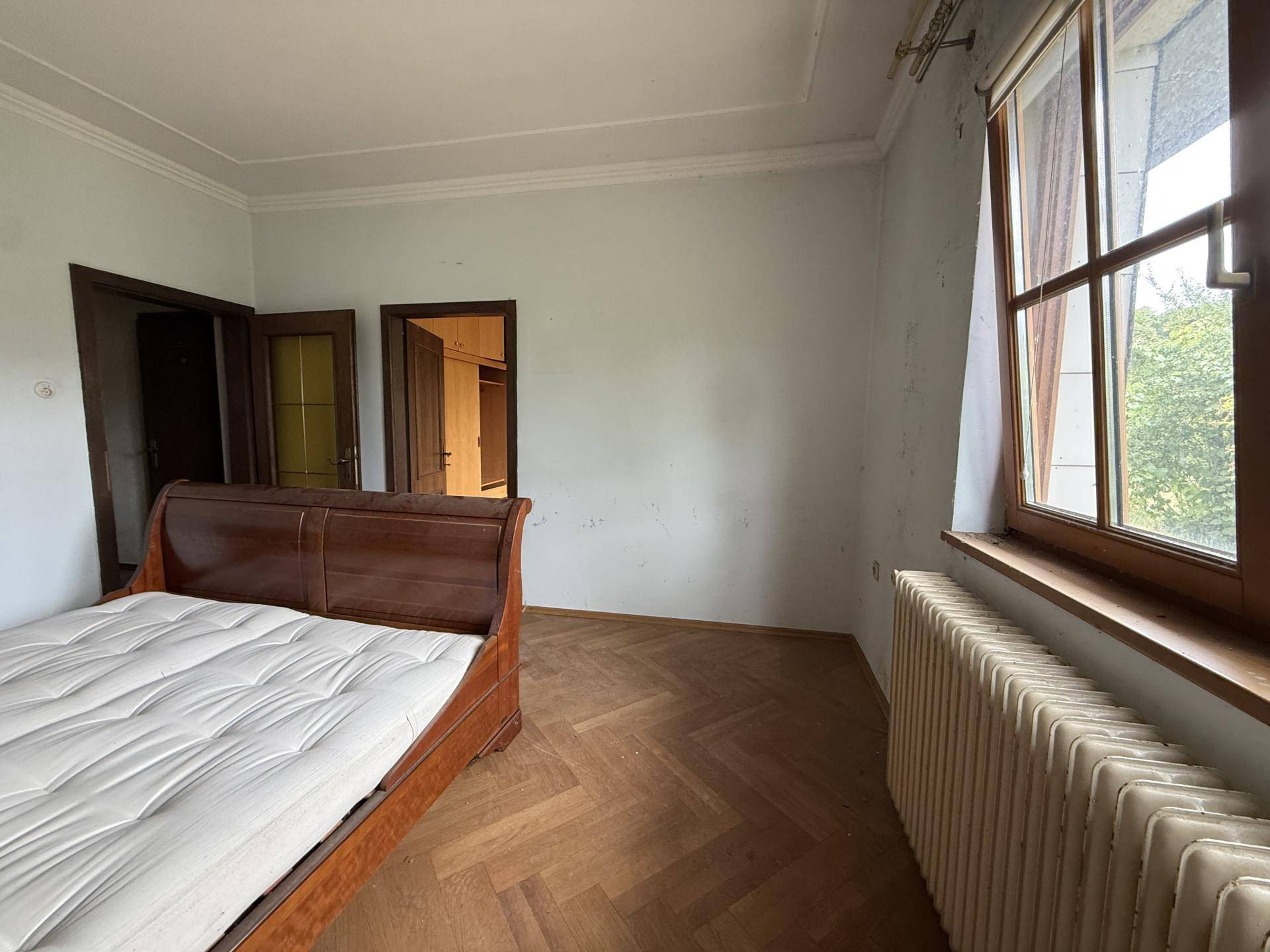 Ein Schlafzimmer mit Holzbett, Heizkörper und Fischgrätparkett, das auf Renovierung wartet.