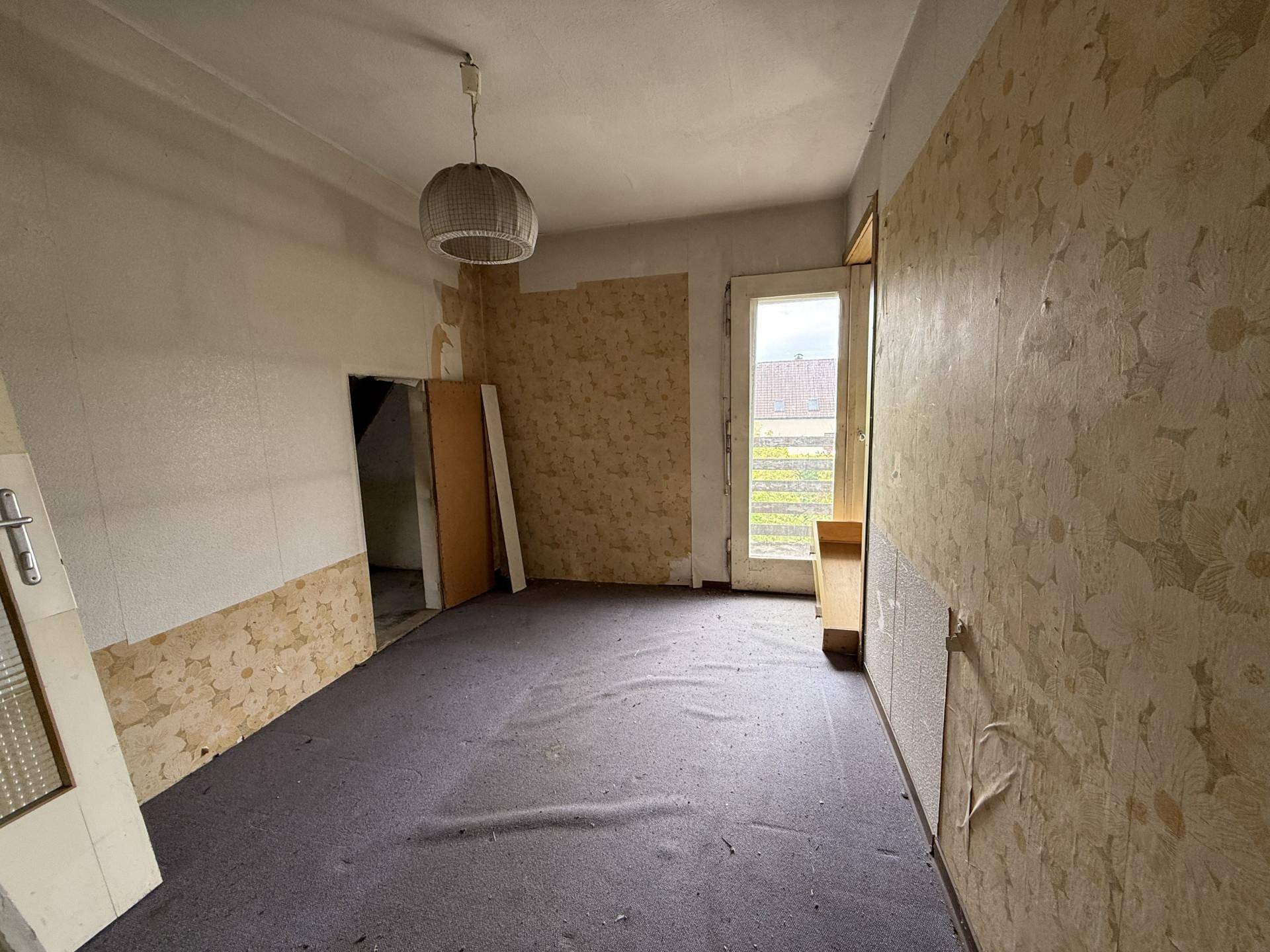 Renovierungsbedürftiger Raum mit abgenutztem Teppichboden und teilweise entfernter Tapete, bereit für die Sanierung.