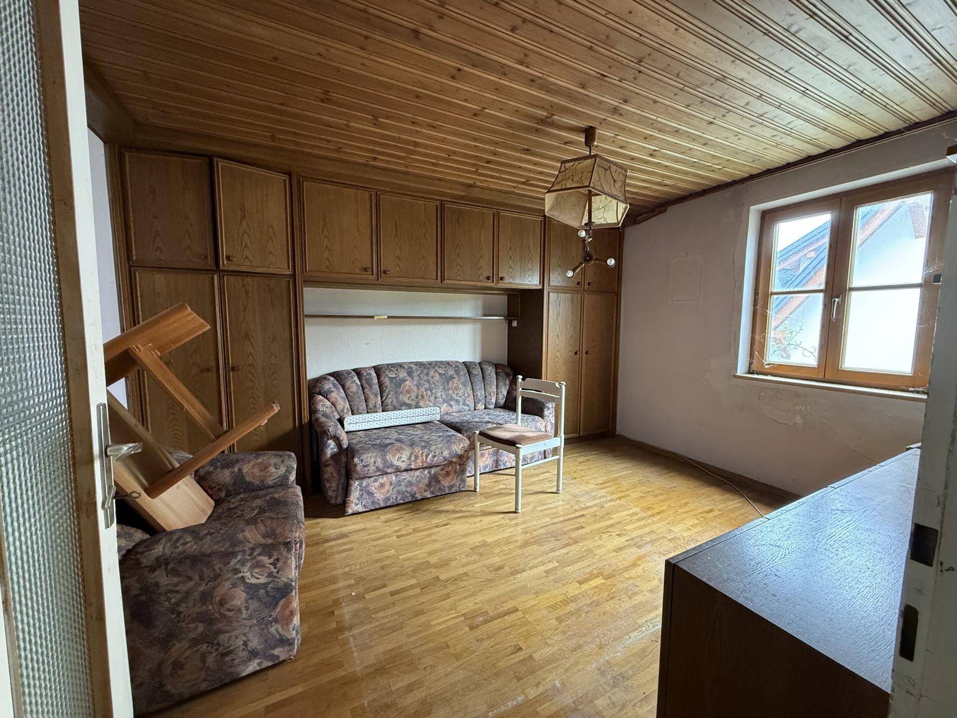 Wohnzimmer mit Holzdecke, Einbauschränken und älteren Möbeln, das eine Renovierung benötigt.