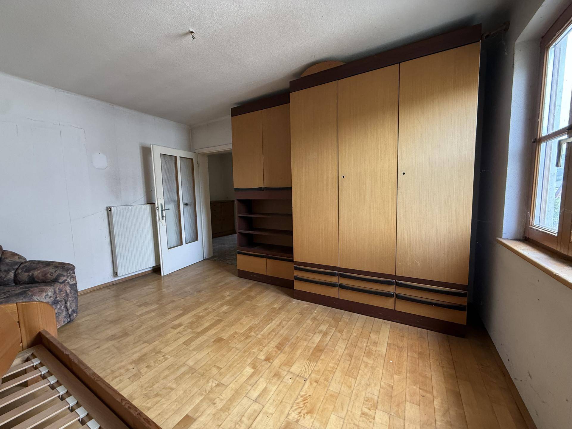 Schlafzimmer mit Holzschrank und Parkettboden, das auf eine Modernisierung wartet.