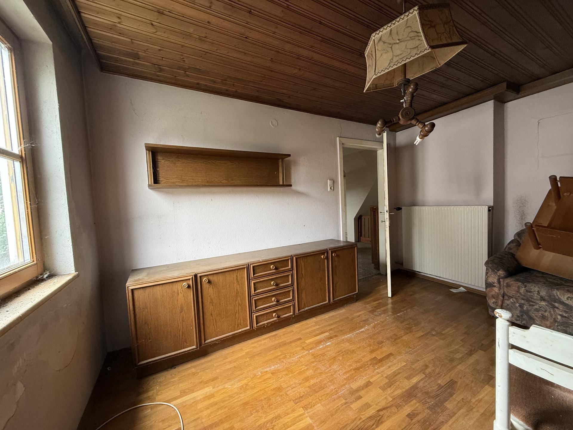 Wohnzimmer mit Holzdecke und Holzmöbeln, das eine umfassende Modernisierung erfordert.