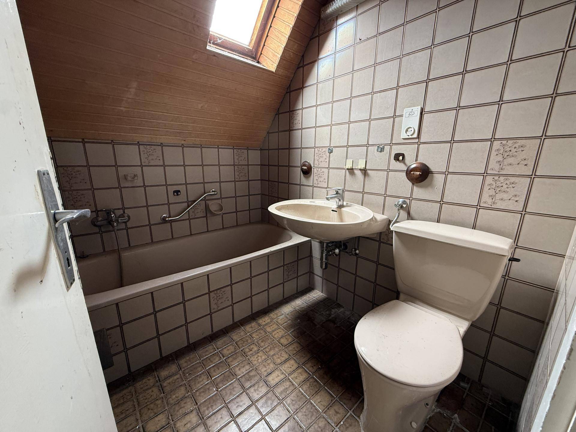 Badezimmer mit Dachschräge, Badewanne und WC, das eine vollständige Renovierung benötigt.