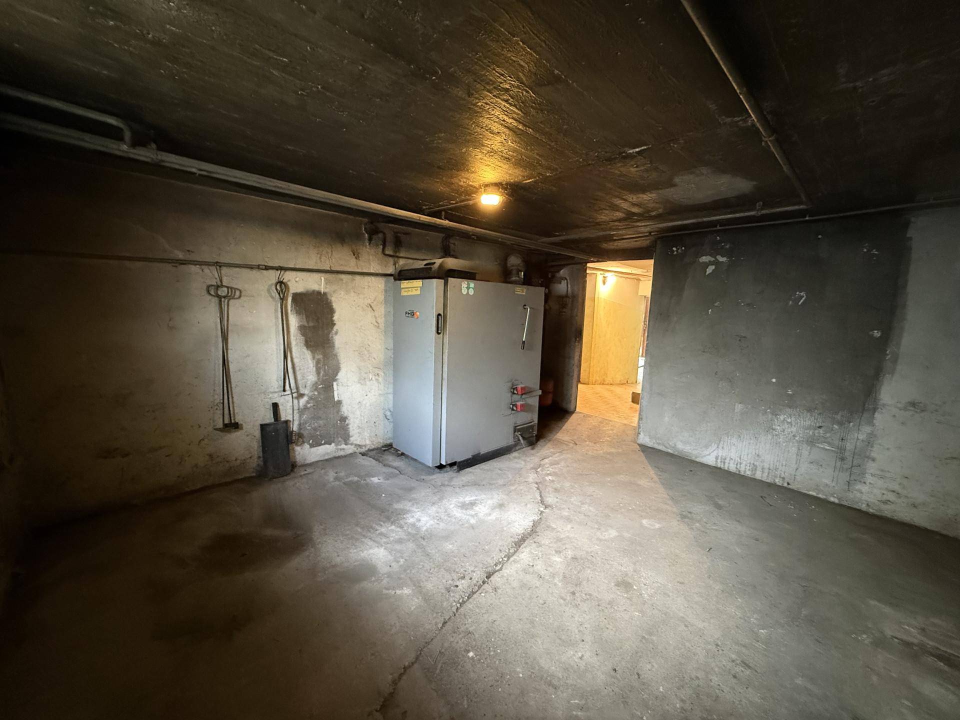 Dunkler Kellerraum mit Betonboden und Heizungsanlage, der zusätzlichen Stauraum bietet.