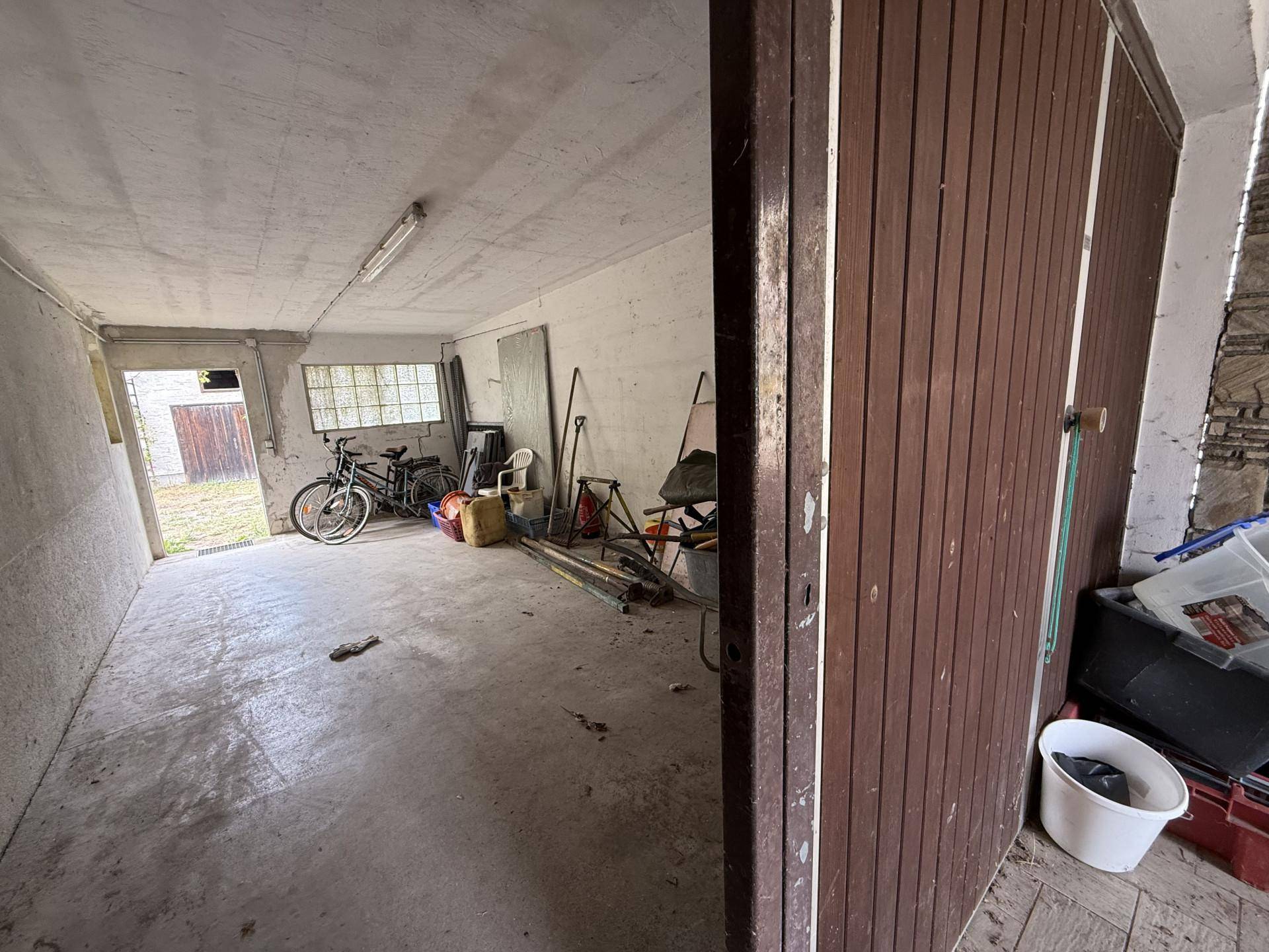 Garage mit Holztor und Betonboden, die zusätzlichen Stauraum und Parkmöglichkeiten bietet.