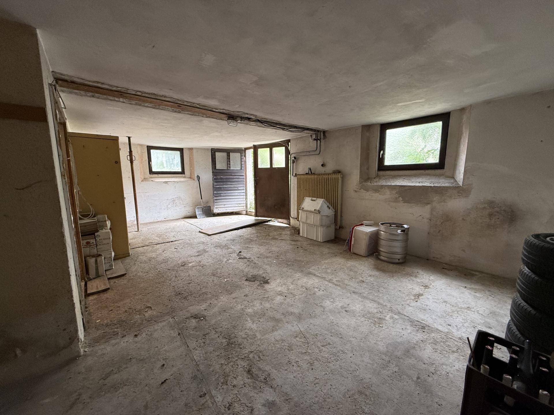 Große Garage mit Betonboden und Fenstern, die viel Platz für Fahrzeuge und Werkzeuge bietet.