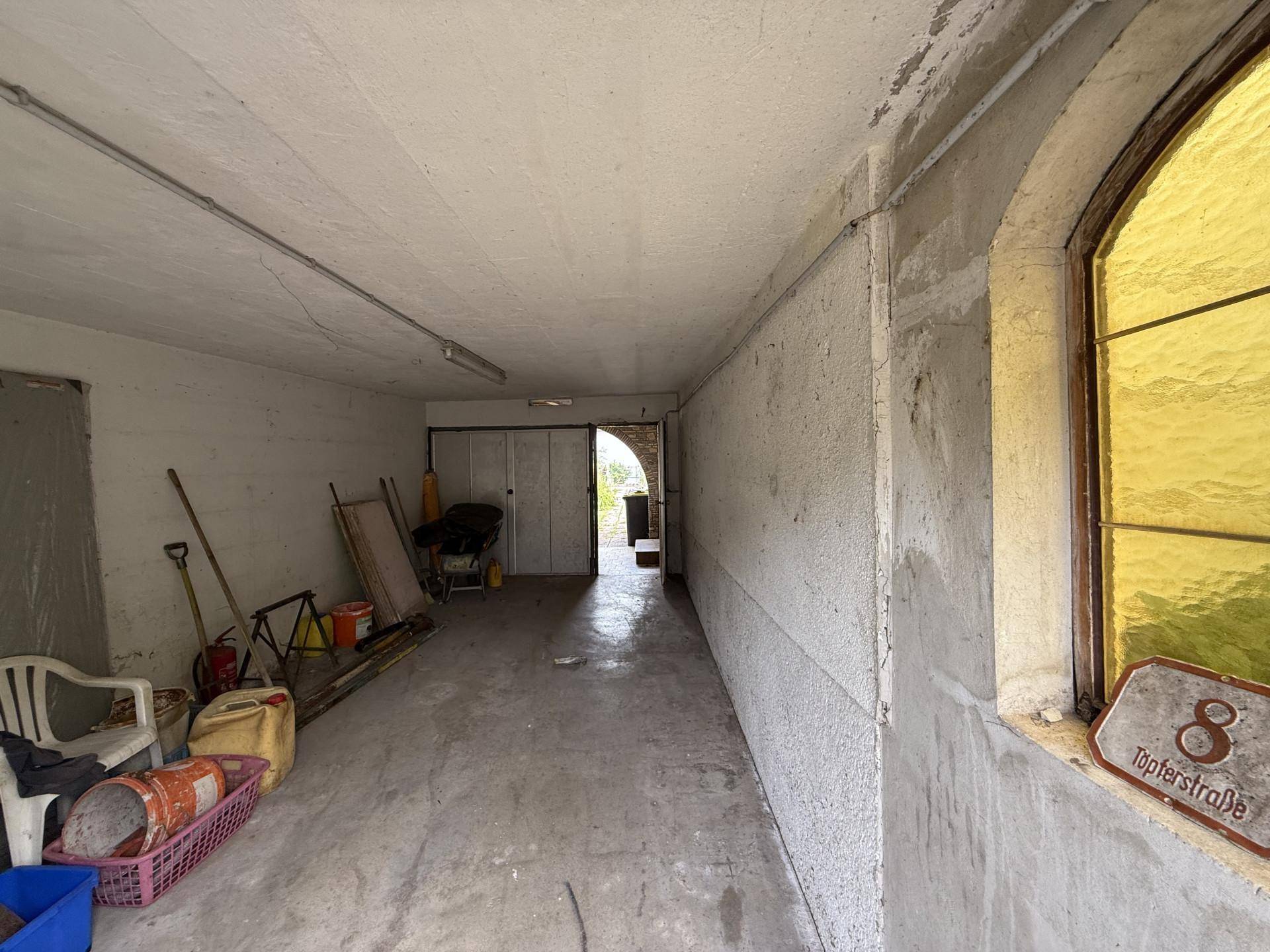 Langer Garagenbereich mit Betonboden und gelbem Fenster, der vielseitig genutzt werden kann.