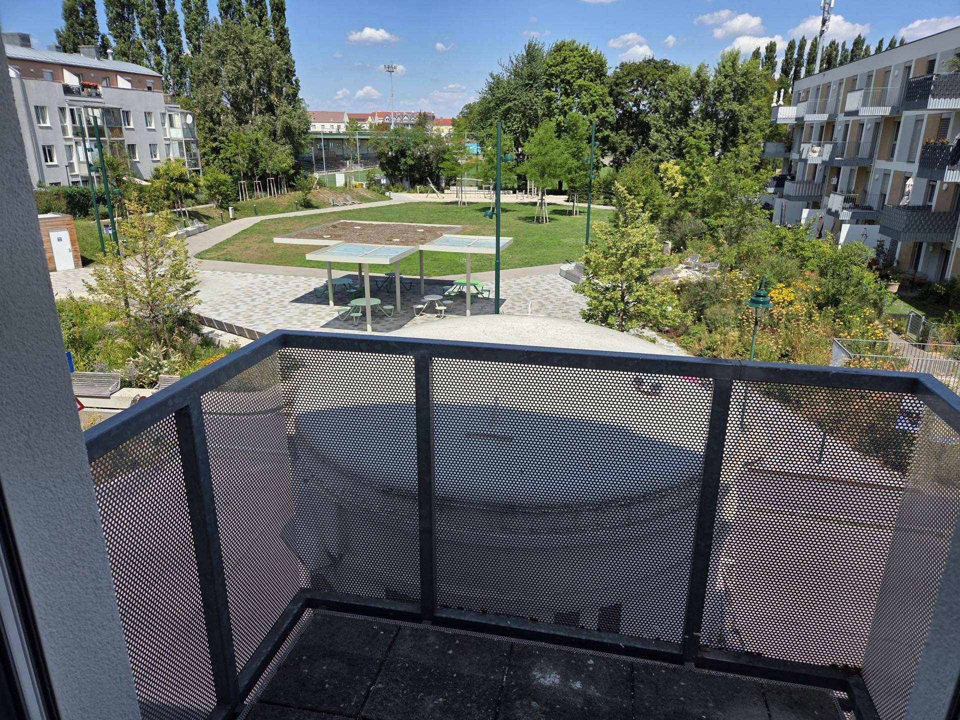 Blick vom Balkon auf eine grüne Gemeinschaftsfläche mit Spielplatz und umliegenden Gebäuden.