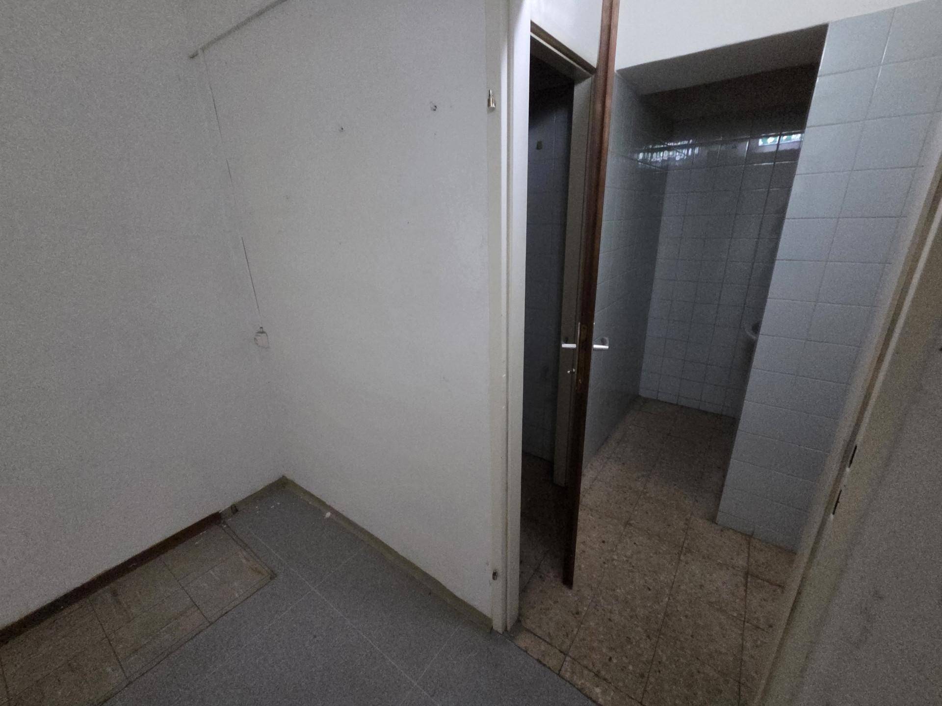 Einfacher Innenraum mit Fliesenboden und Zugang zu einem gefliesten Bereich, möglicherweise einer Toilette oder Dusche.