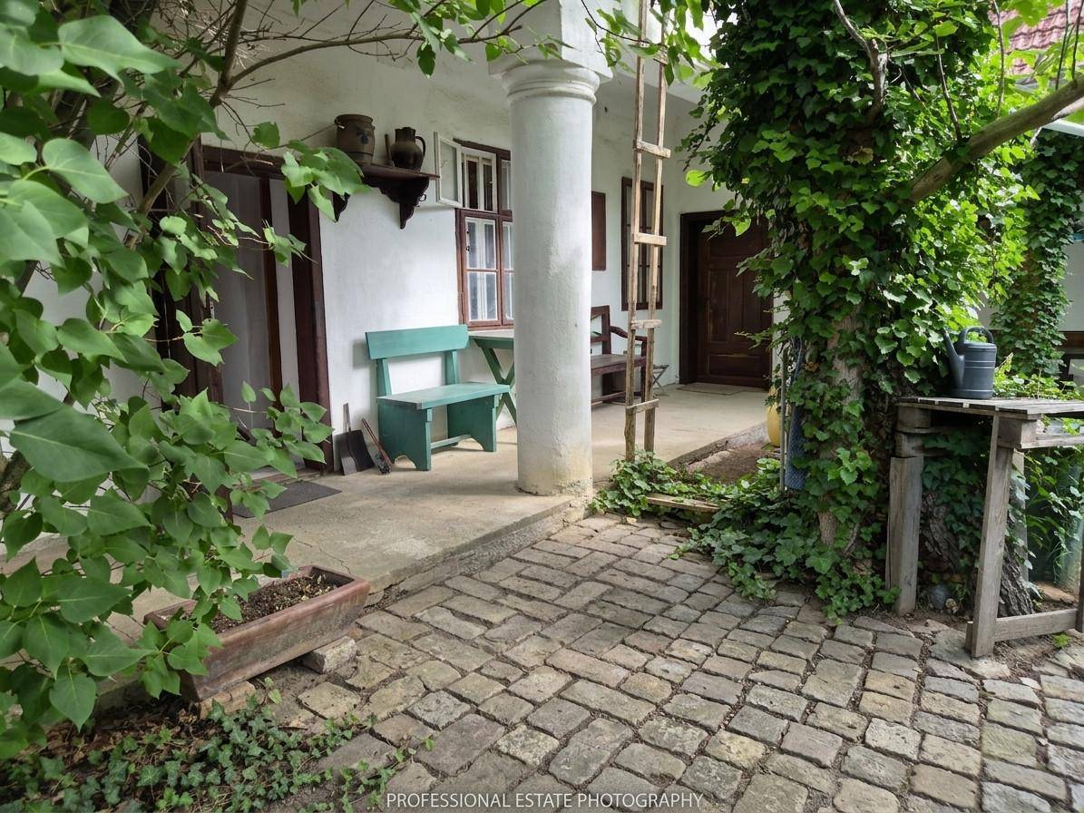 Überdachter Außenbereich mit Kopfsteinpflaster, Säule und üppiger Begrünung im Innenhof.