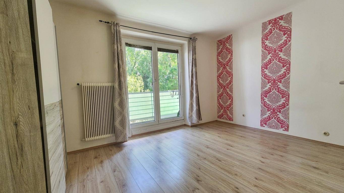 Schlafzimmer mit Holzboden, dekorativer Tapete und Fenster mit Blick ins Grüne.