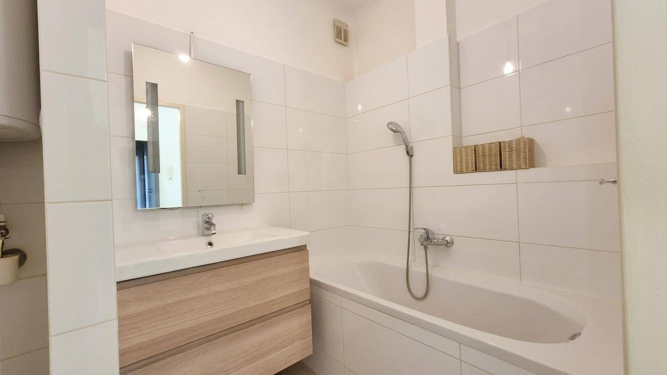 Modern gefliestes Badezimmer mit Badewanne, Waschbecken und Spiegelschrank.