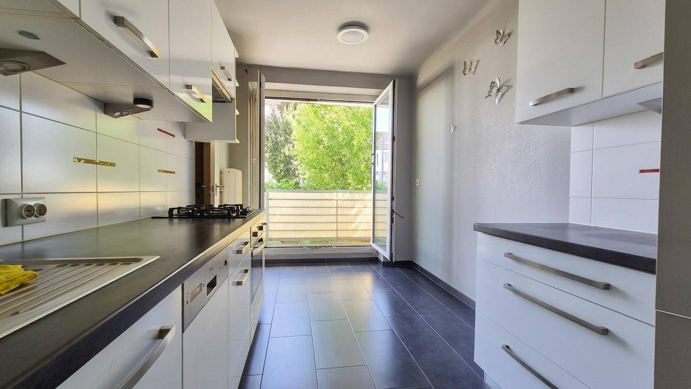 Funktionale Küche mit weißen Schränken, dunkler Arbeitsplatte und Zugang zum Balkon.