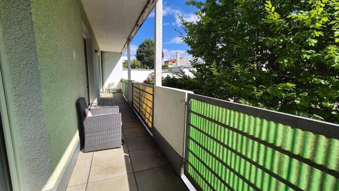 Langer Balkon mit Sitzgelegenheit, Fliesenboden und grüner Sichtschutzwand.