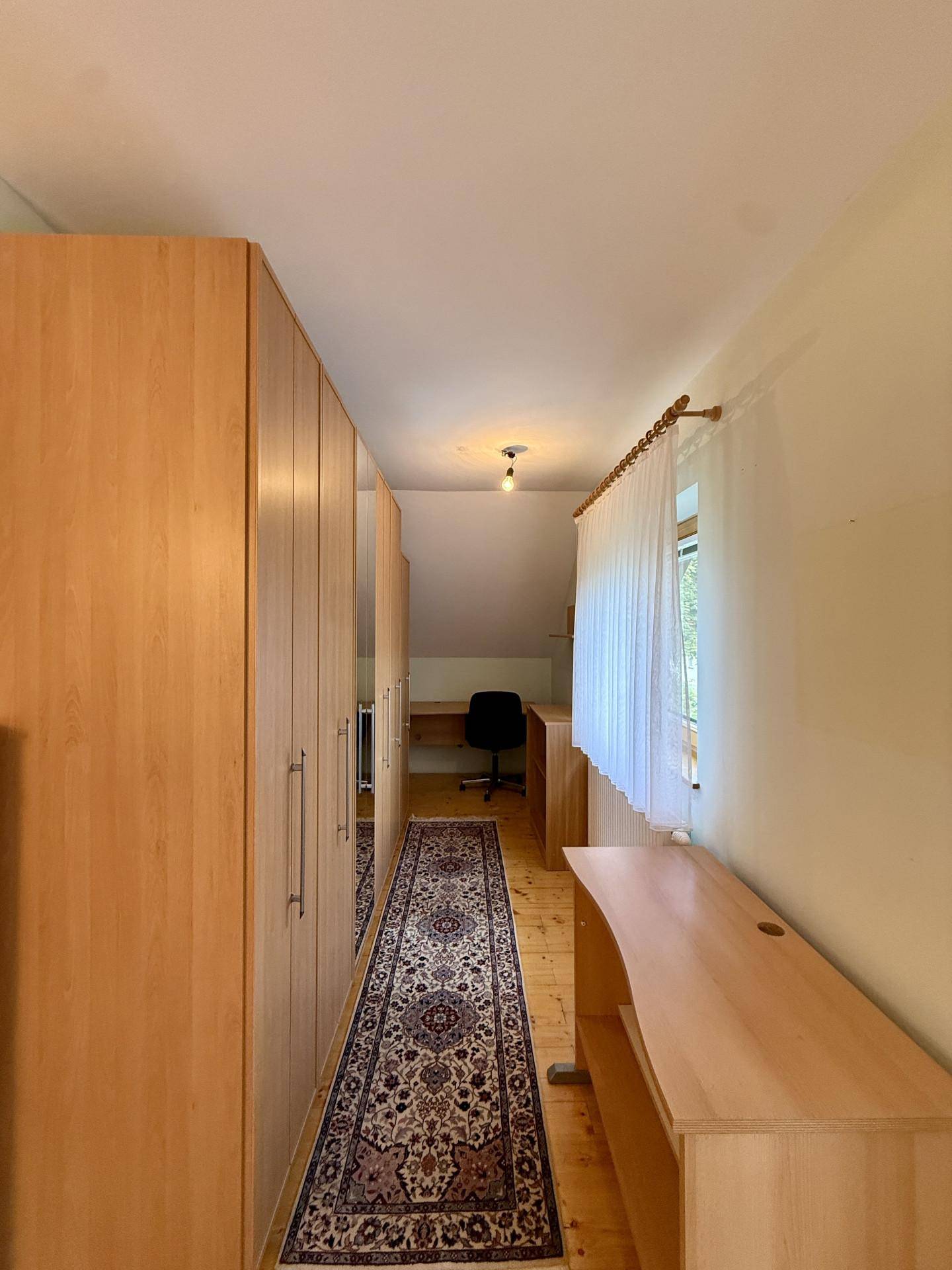 Langer Raum mit Einbauschränken, Schreibtisch und Fenster, ideal als Büro.