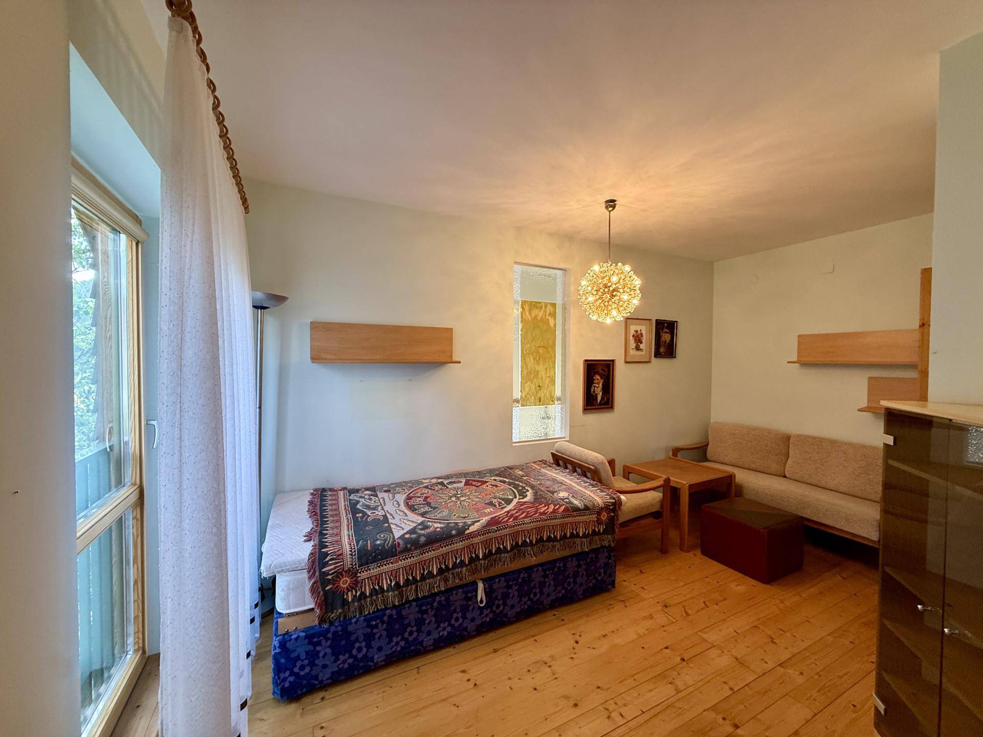 Schlafzimmer mit Holzboden, großem Fenster und einfacher Einrichtung.