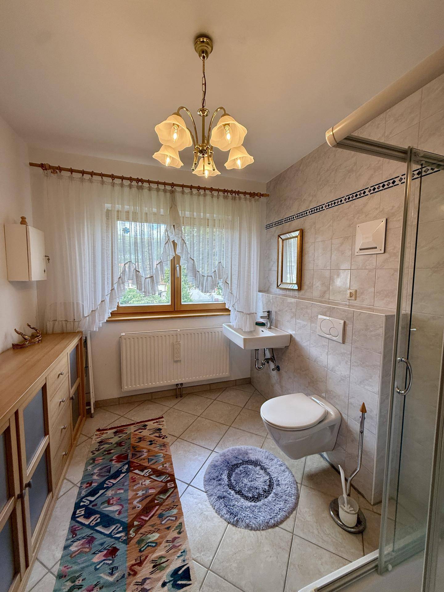 Gefliestes Badezimmer mit Dusche, WC, Waschbecken und Fenster.