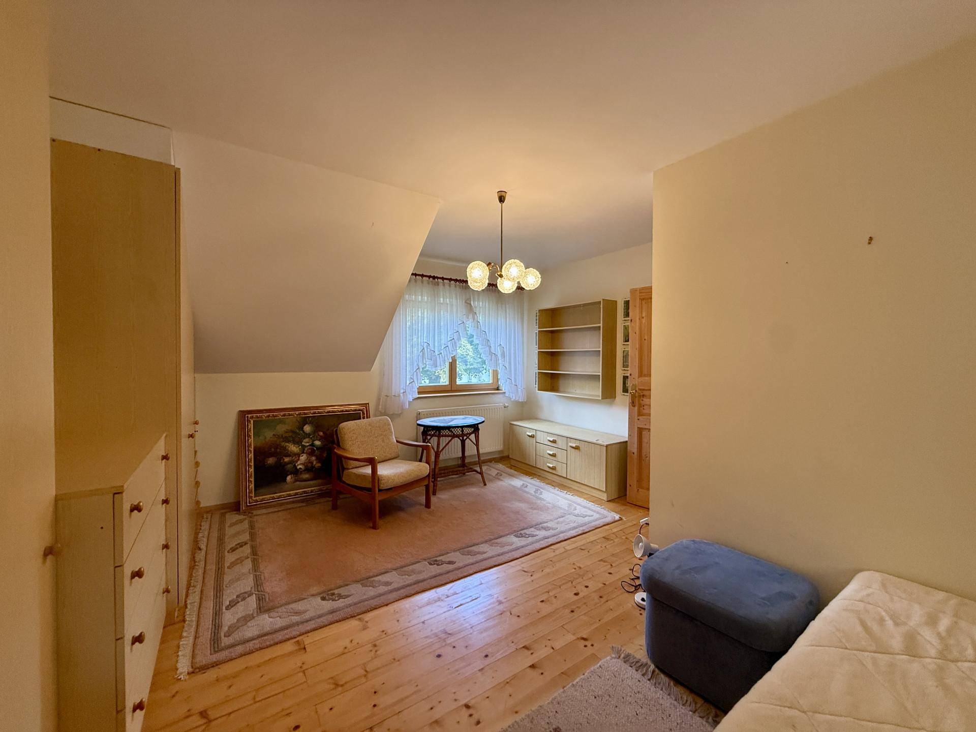 Gemütliches Zimmer im Dachgeschoss mit Holzboden, Schrägen und Fenster.