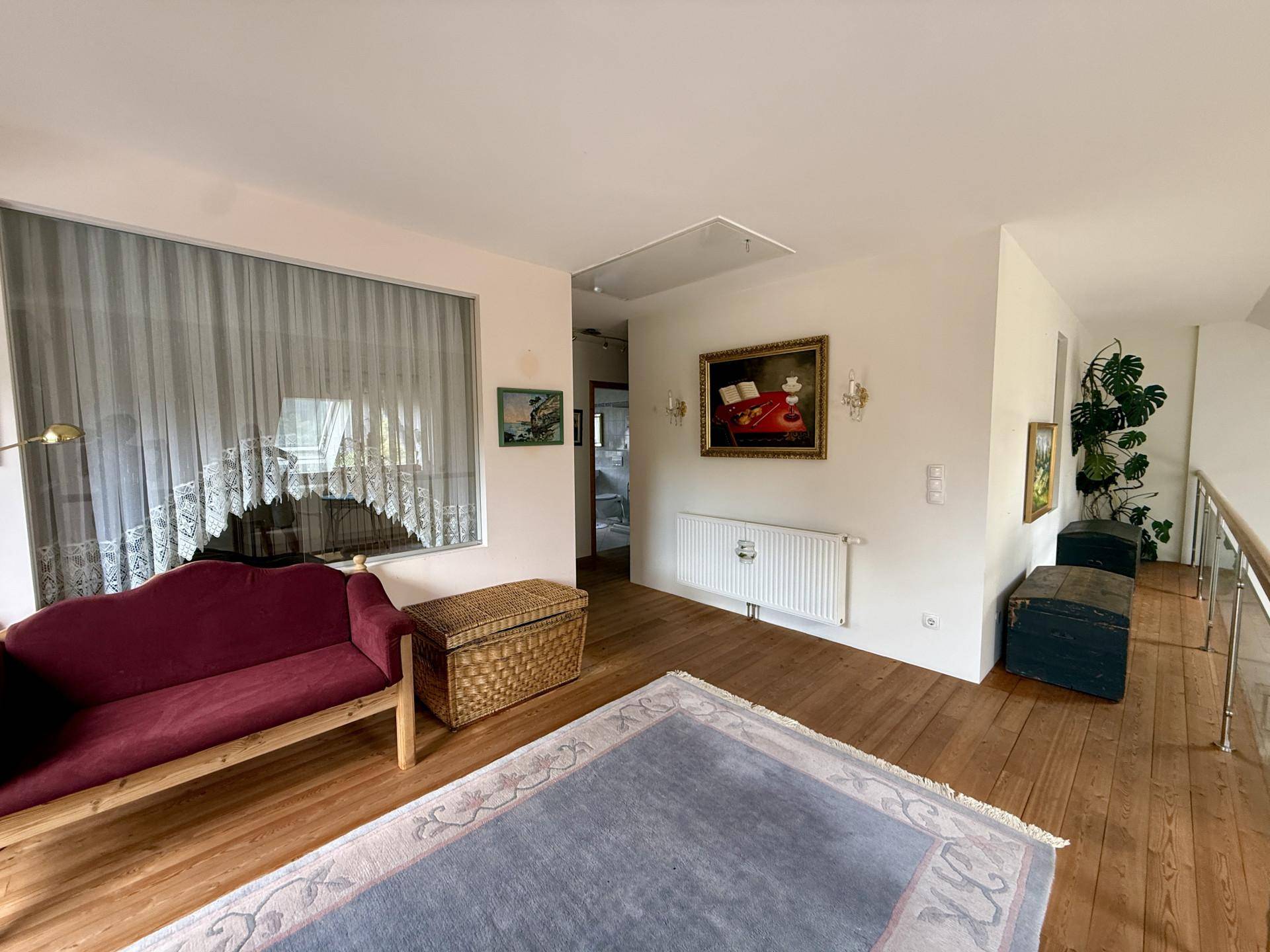 Offener Wohnbereich im Obergeschoss mit Holzboden, Sofa und Blick auf den unteren Bereich.