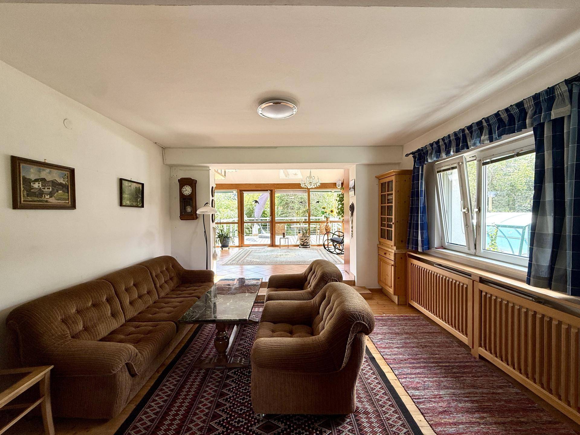 Traditionelles Wohnzimmer mit bequemen Sofas, Teppichboden und Zugang zu einem hellen Bereich.