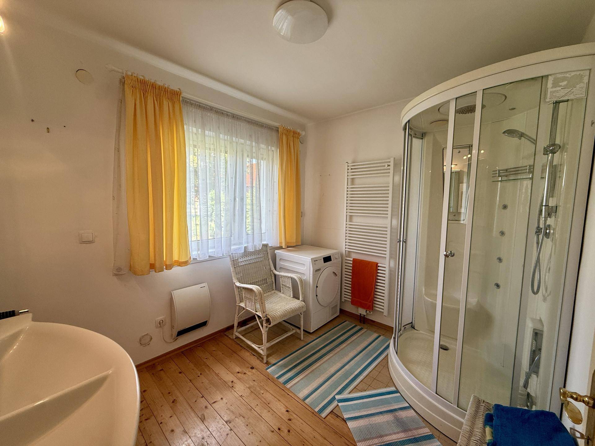 Badezimmer mit Duschkabine, Waschmaschine, Holzfußboden und Fenster.