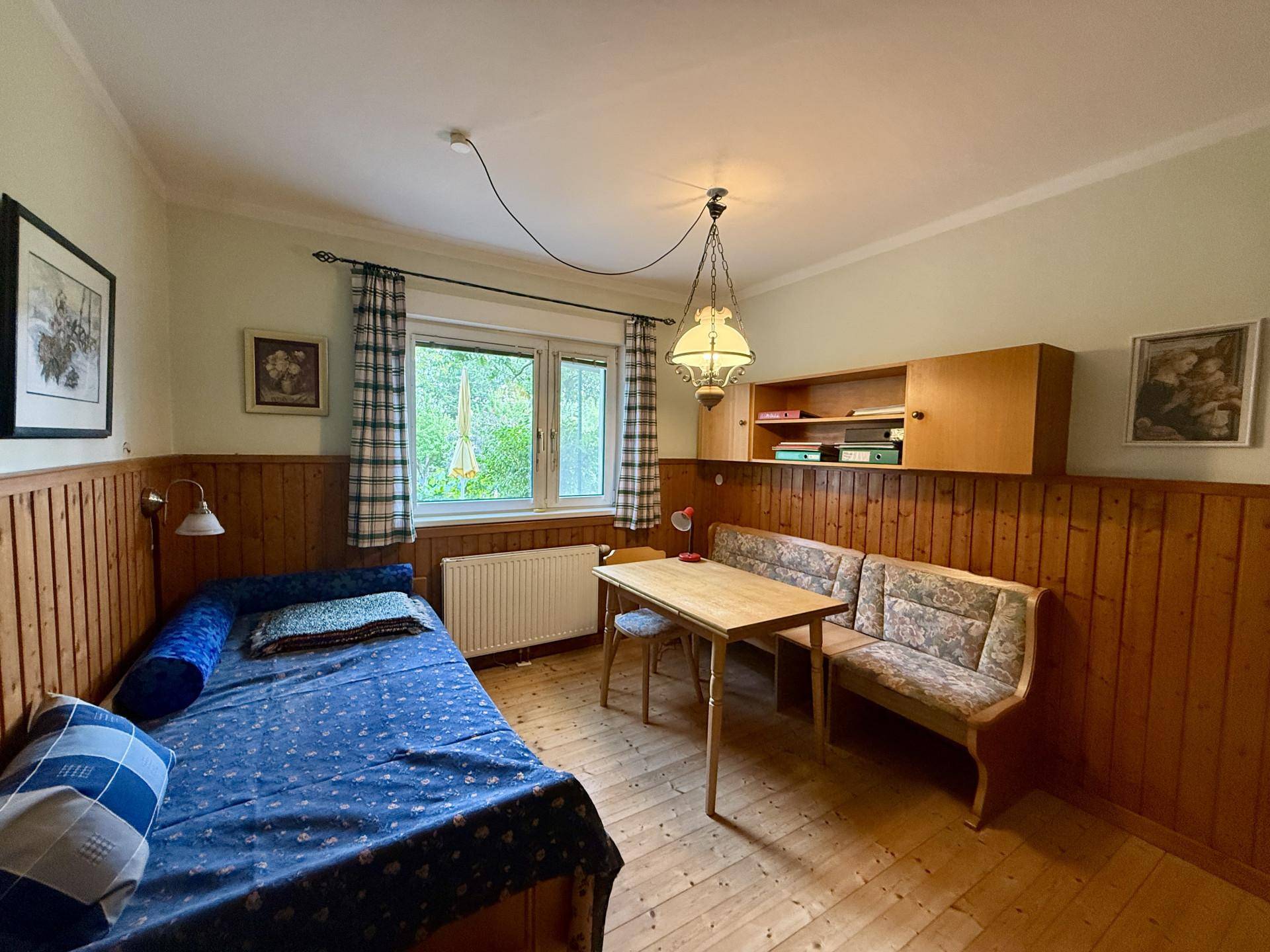 Schlafzimmer mit Holzvertäfelung, Einzelbett, Esstisch und Fenster.