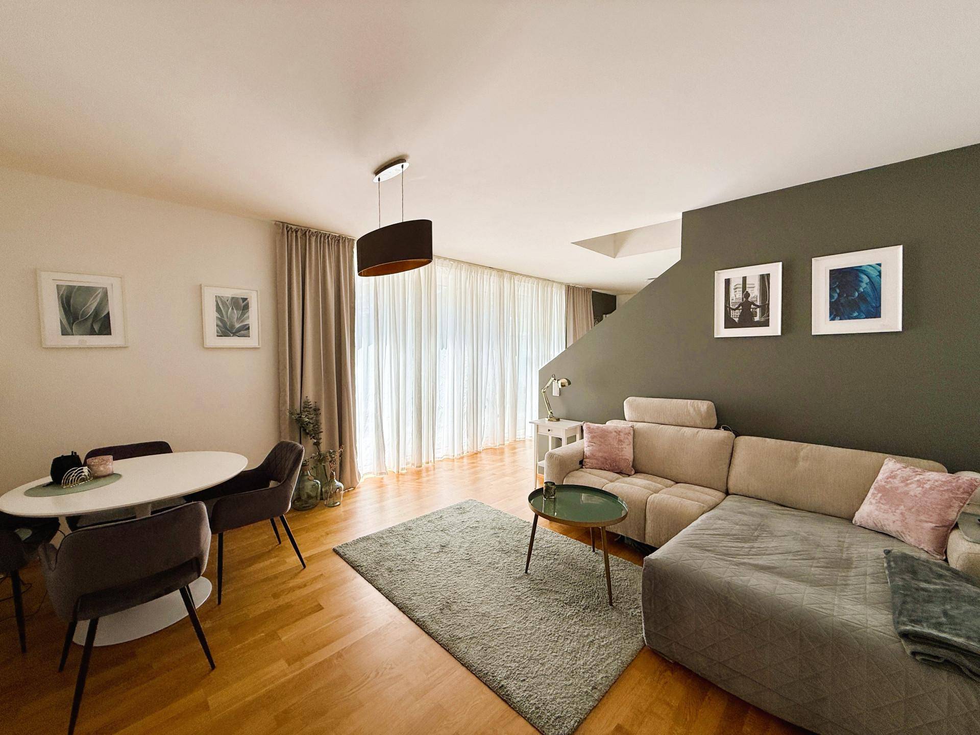 Heller Wohn- und Essbereich mit Holzboden, beiger Couch und modernem Esstisch.