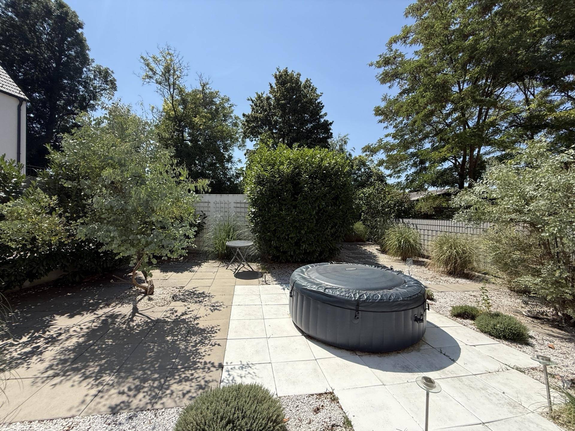Sonniger Gartenbereich mit gepflasterter Terrasse, Whirlpool und üppiger Bepflanzung.