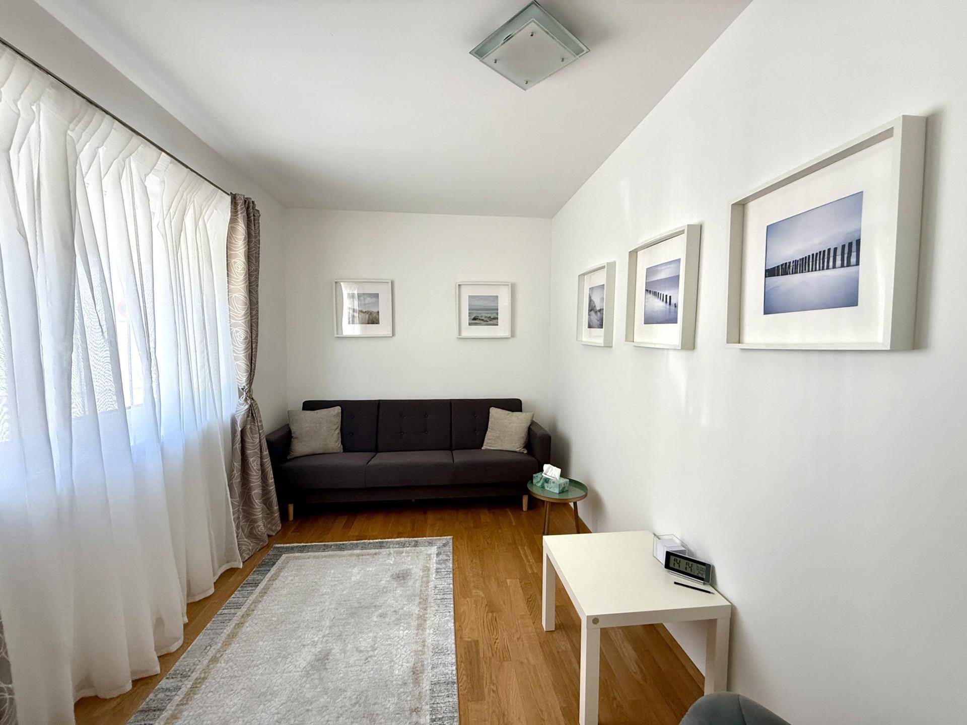 Gemütliches Zimmer mit Sofa, Holzboden und großen Fenstern für viel Tageslicht.