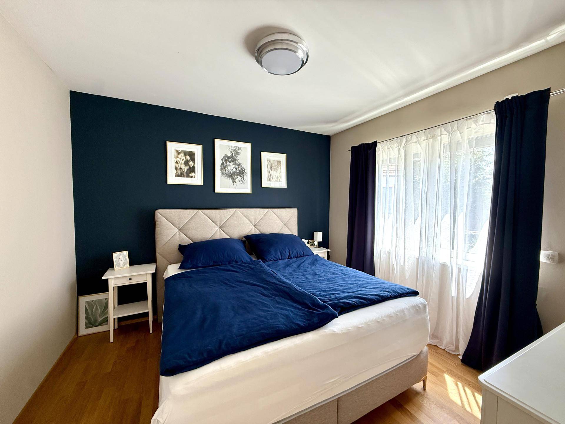 Schlafzimmer mit Doppelbett, dunkelblauer Akzentwand und Holzboden.