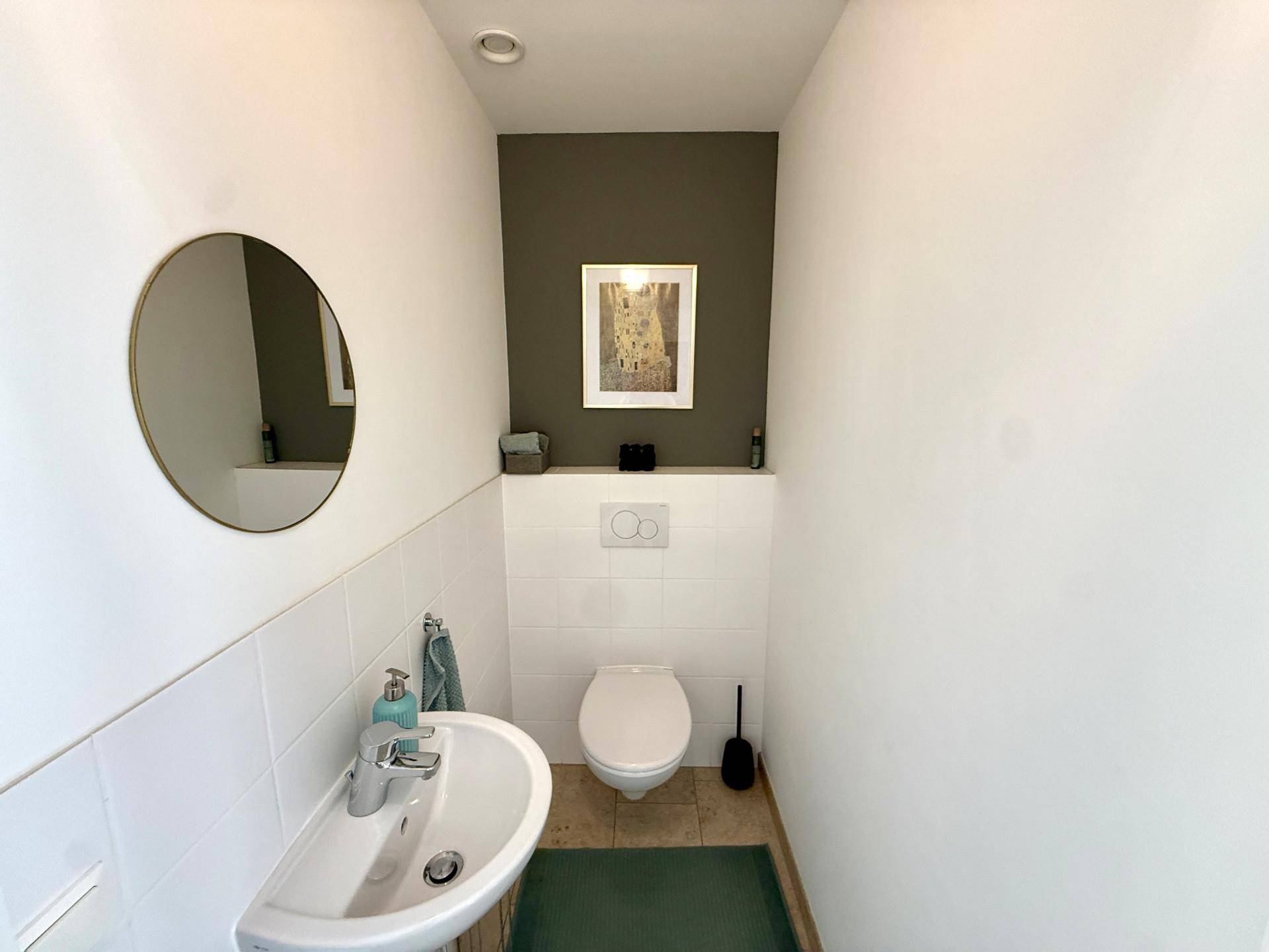 Modernes Gäste-WC mit Wand-WC, kleinem Waschbecken und runden Spiegel.