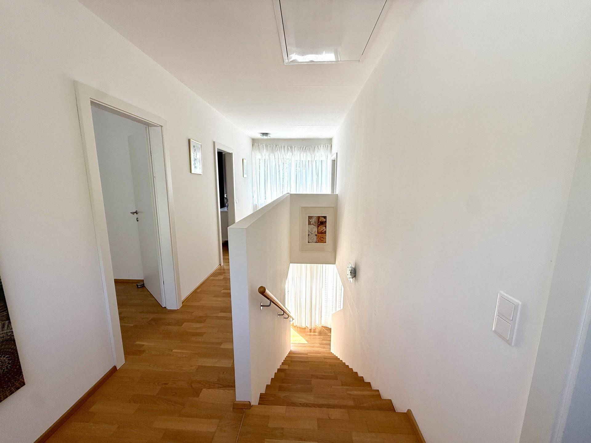 Heller Flur mit Holztreppe, Holzboden und Zugang zu weiteren Zimmern.
