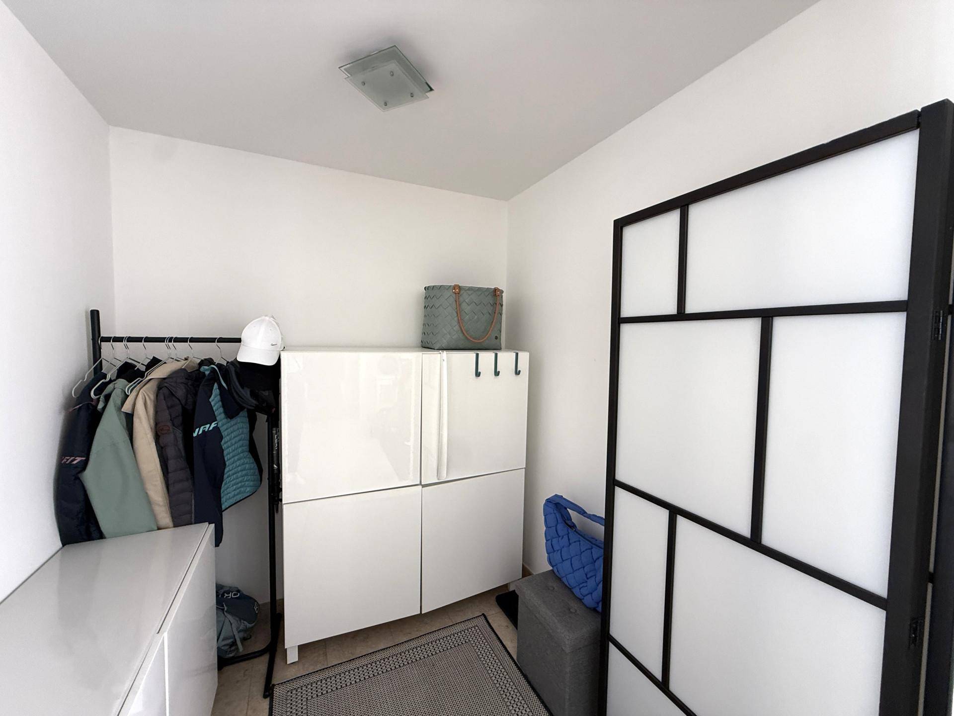 Heller Eingangsbereich mit Garderobe, weißem Schrank und modernem Raumteiler.