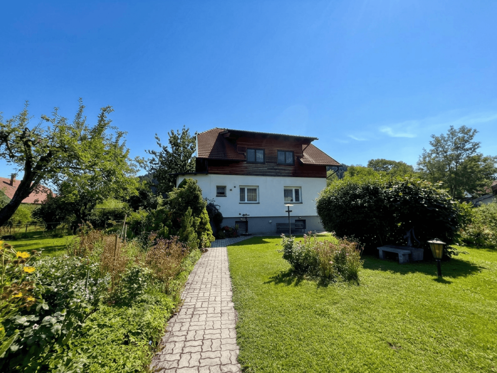 Gepflegter Garten mit Steinweg, Rasenflächen und Blick auf das Wohnhaus.