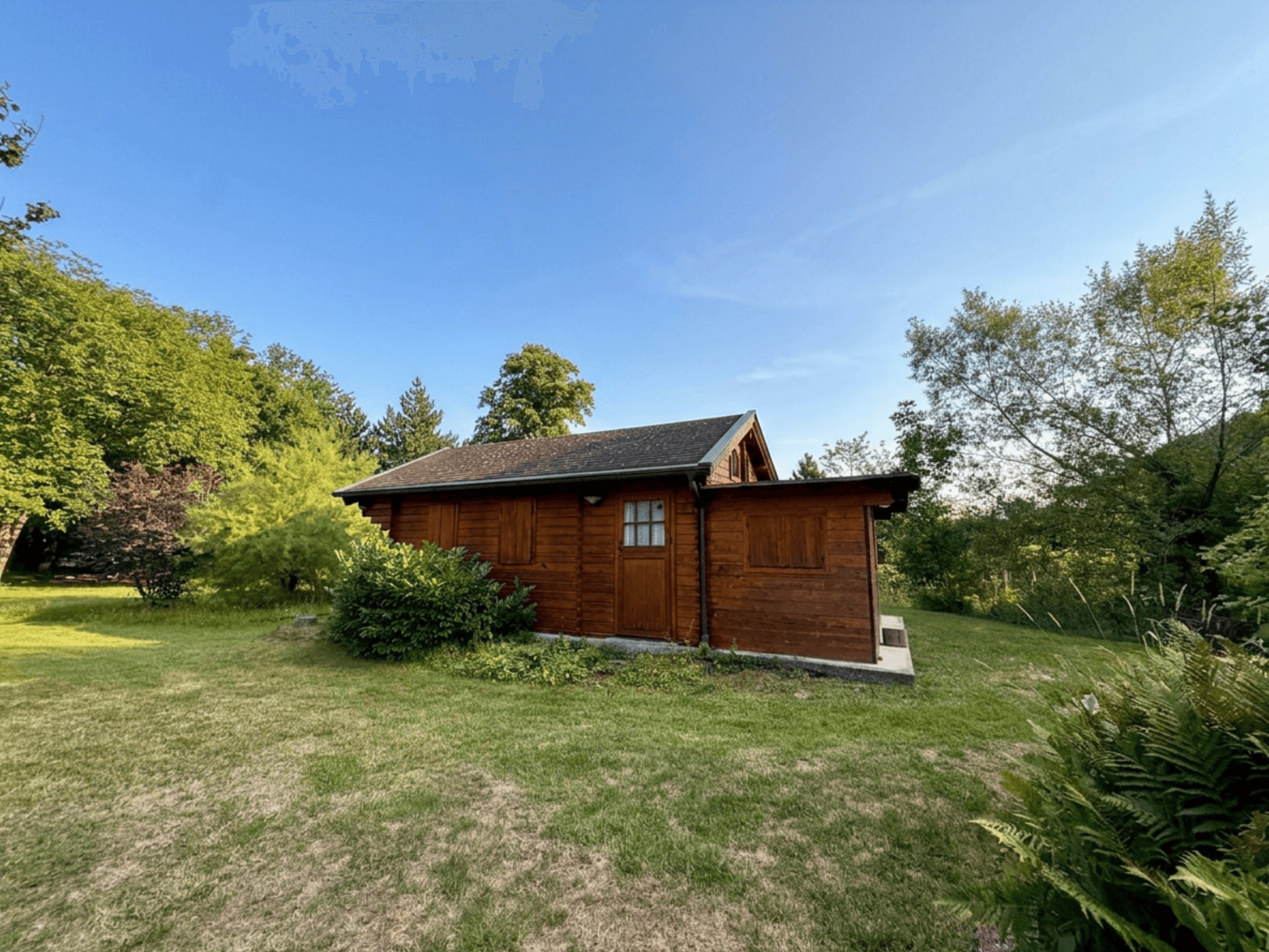 Kleine Holzhütte im Garten, umgeben von Bäumen und Grünflächen.