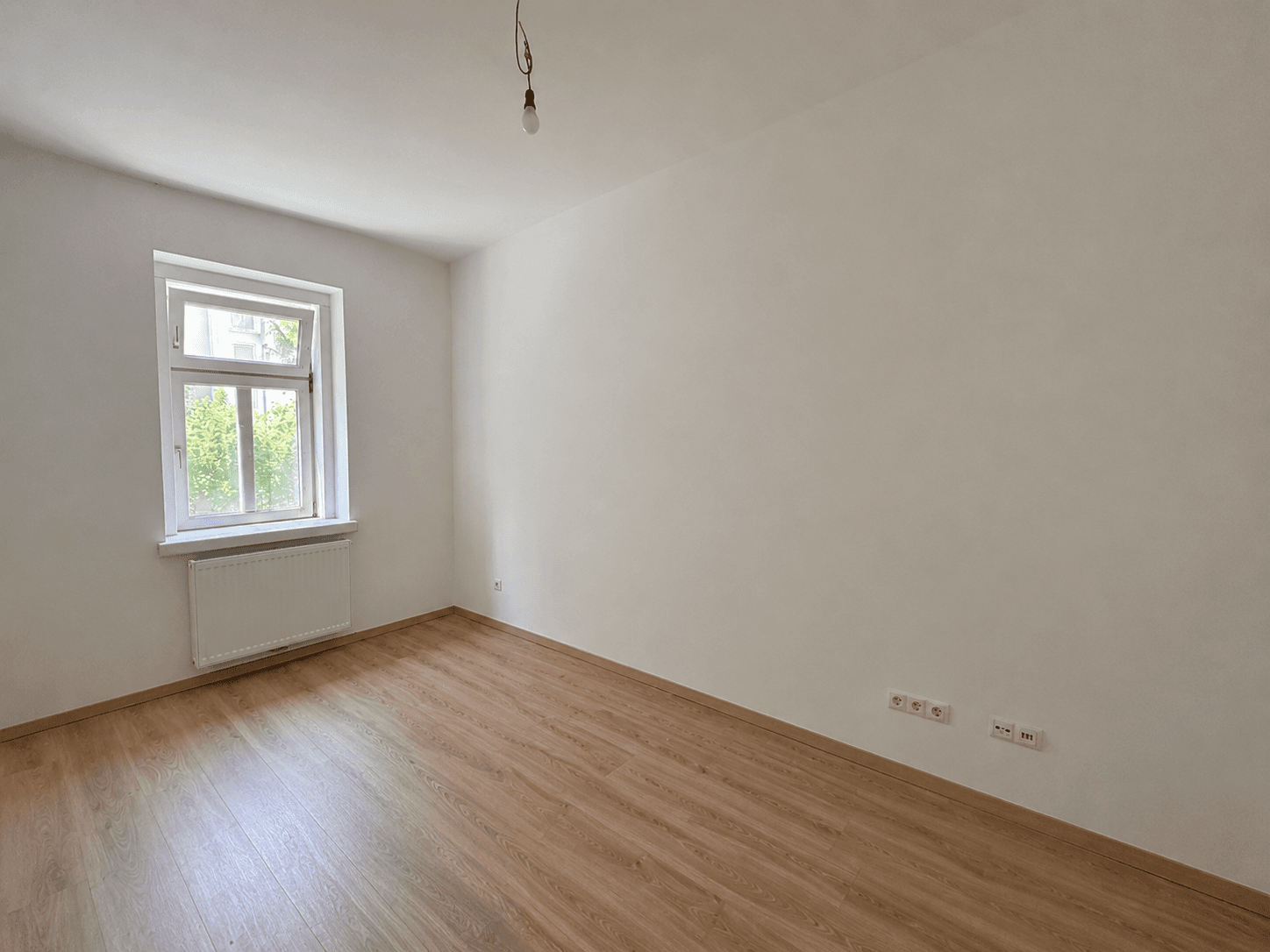 Geräumiges, helles Zimmer mit Laminatboden und einem Fenster, ideal für verschiedene Nutzungen.