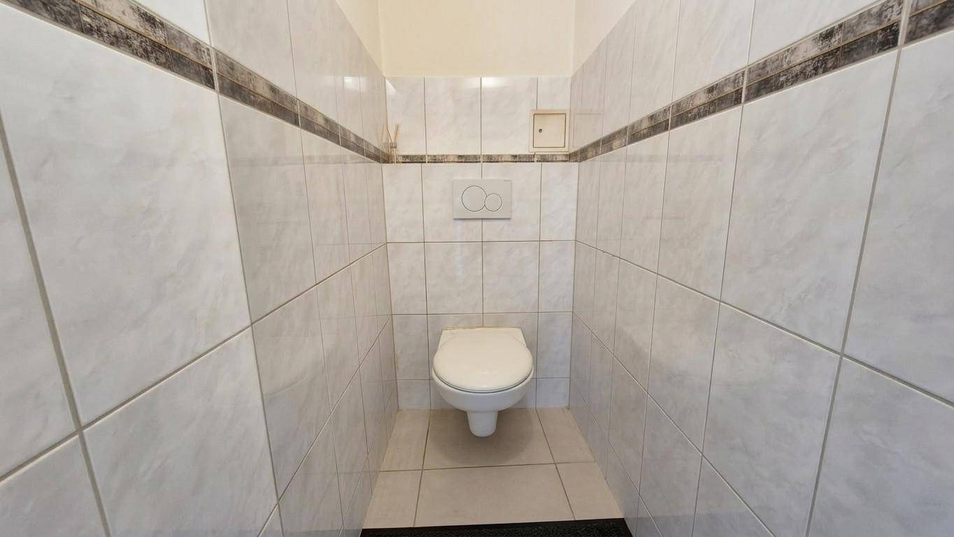 Separate Toilette mit weißen Fliesen und Wand-WC, sauber und funktional.