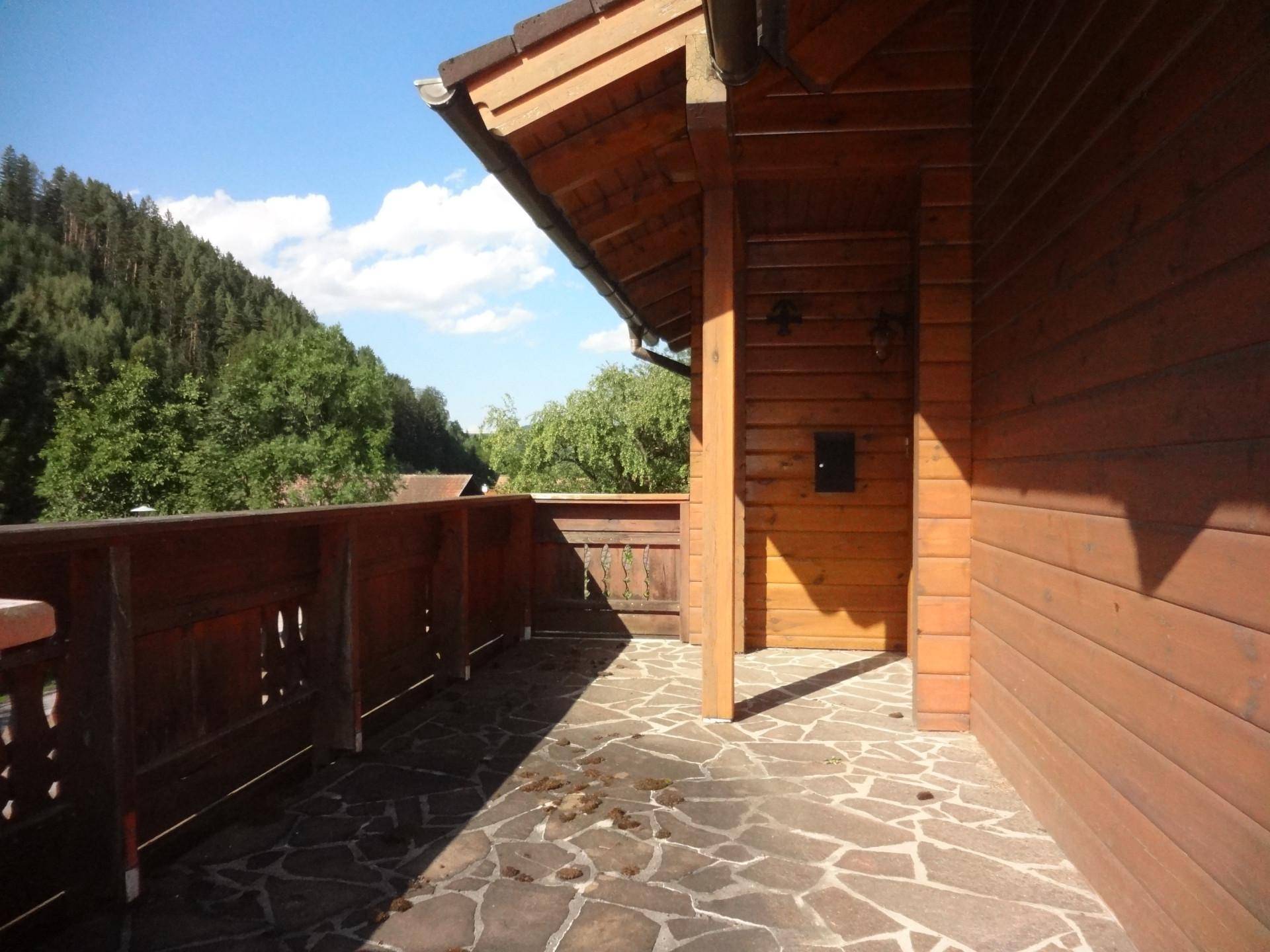 Geräumiger Holzbalkon mit rustikalem Geländer und Steinboden, umgeben von Natur.