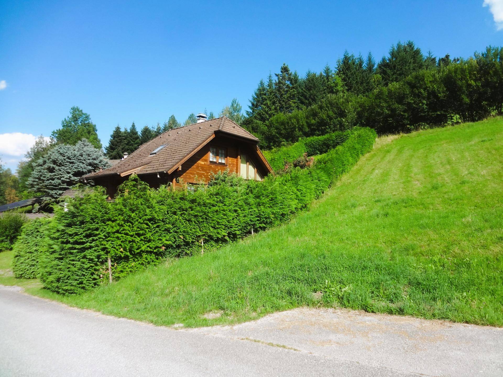 Holzhaus in Hanglage, umgeben von gepflegten Hecken und grünen Wiesen.