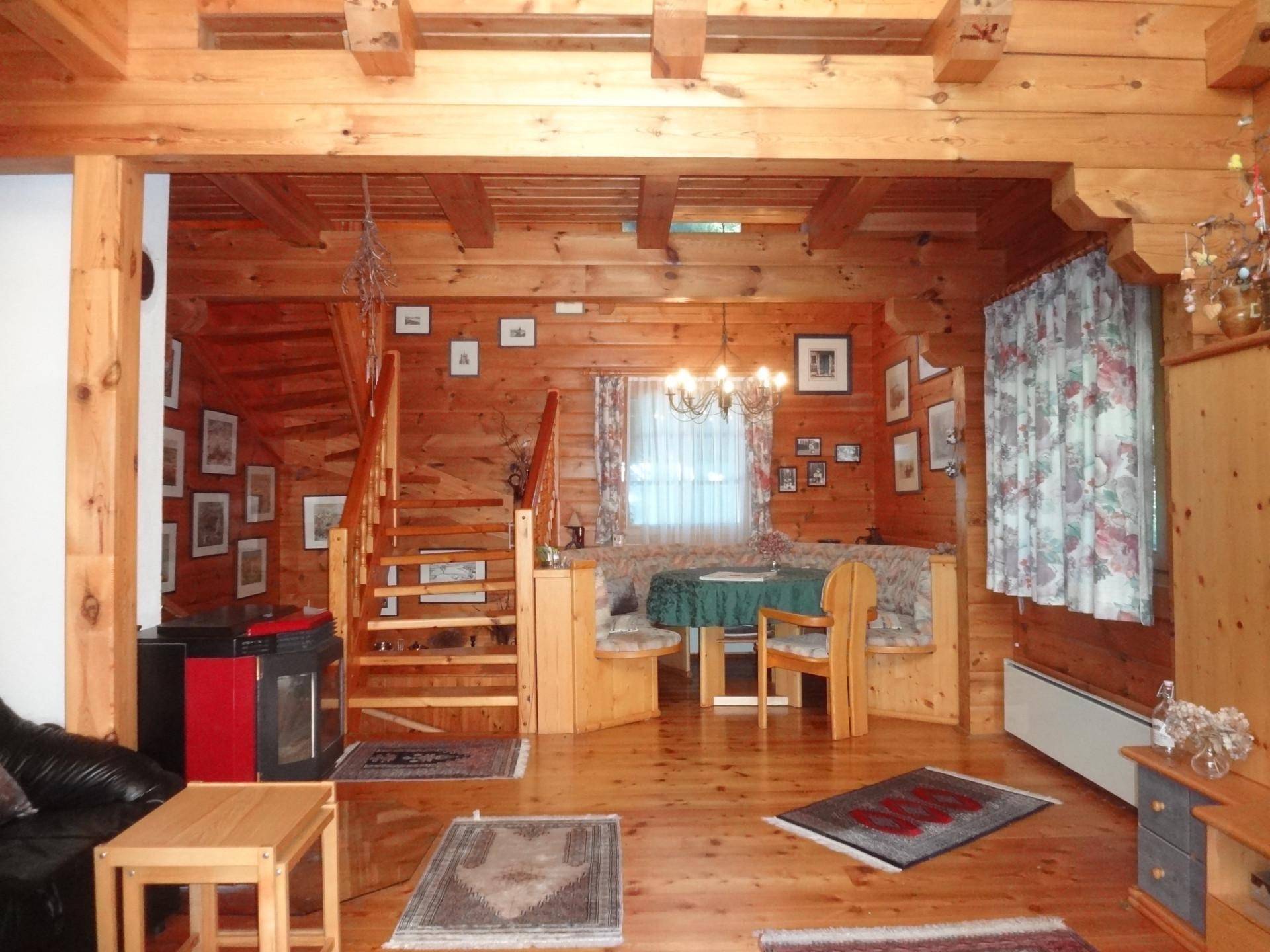 Offener Wohn- und Essbereich mit Holztreppe, Kaminofen und traditioneller Sitzecke.