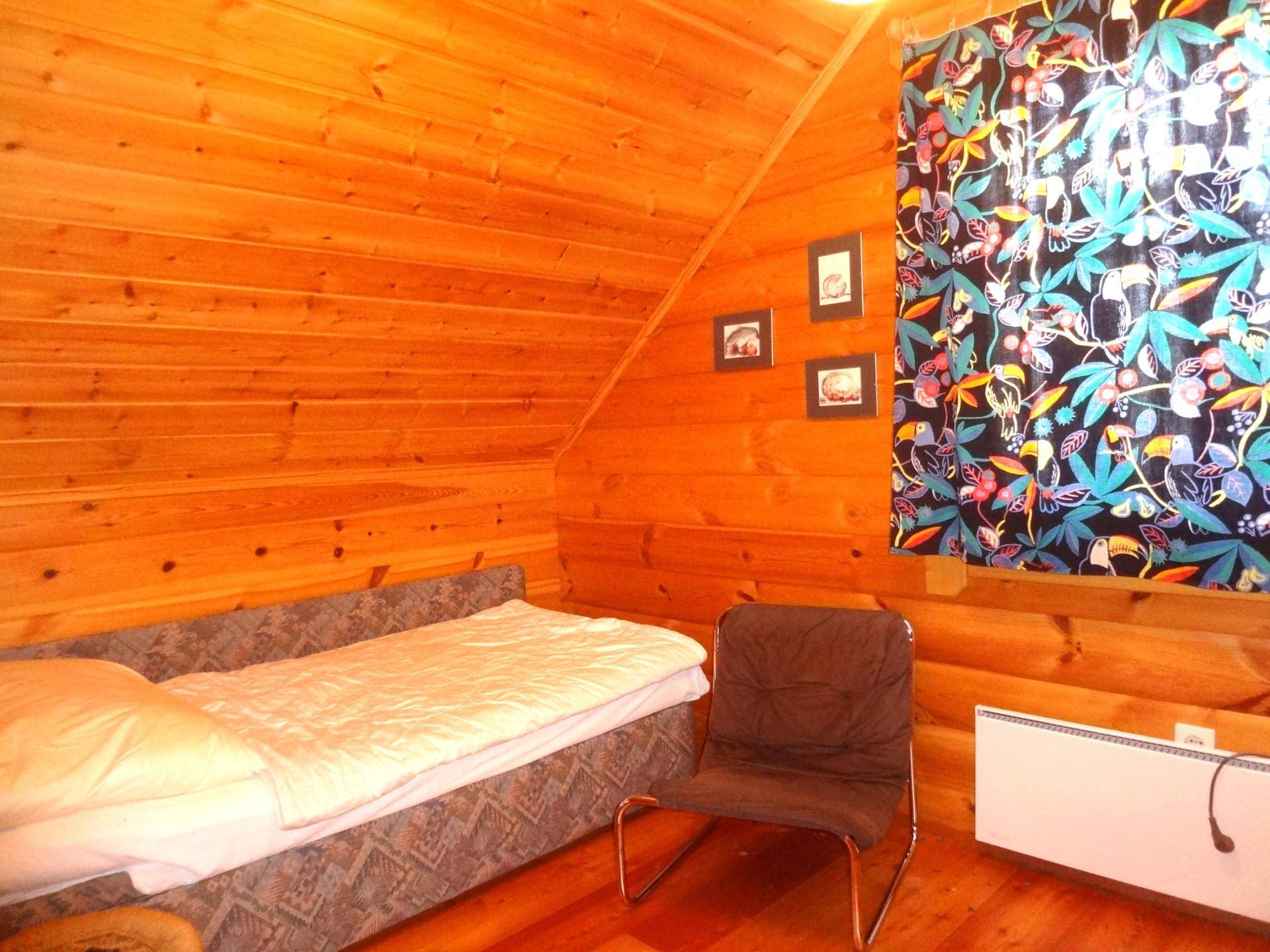 Schlafzimmer mit Holzwänden, Einzelbett und farbenfrohen Vorhängen.