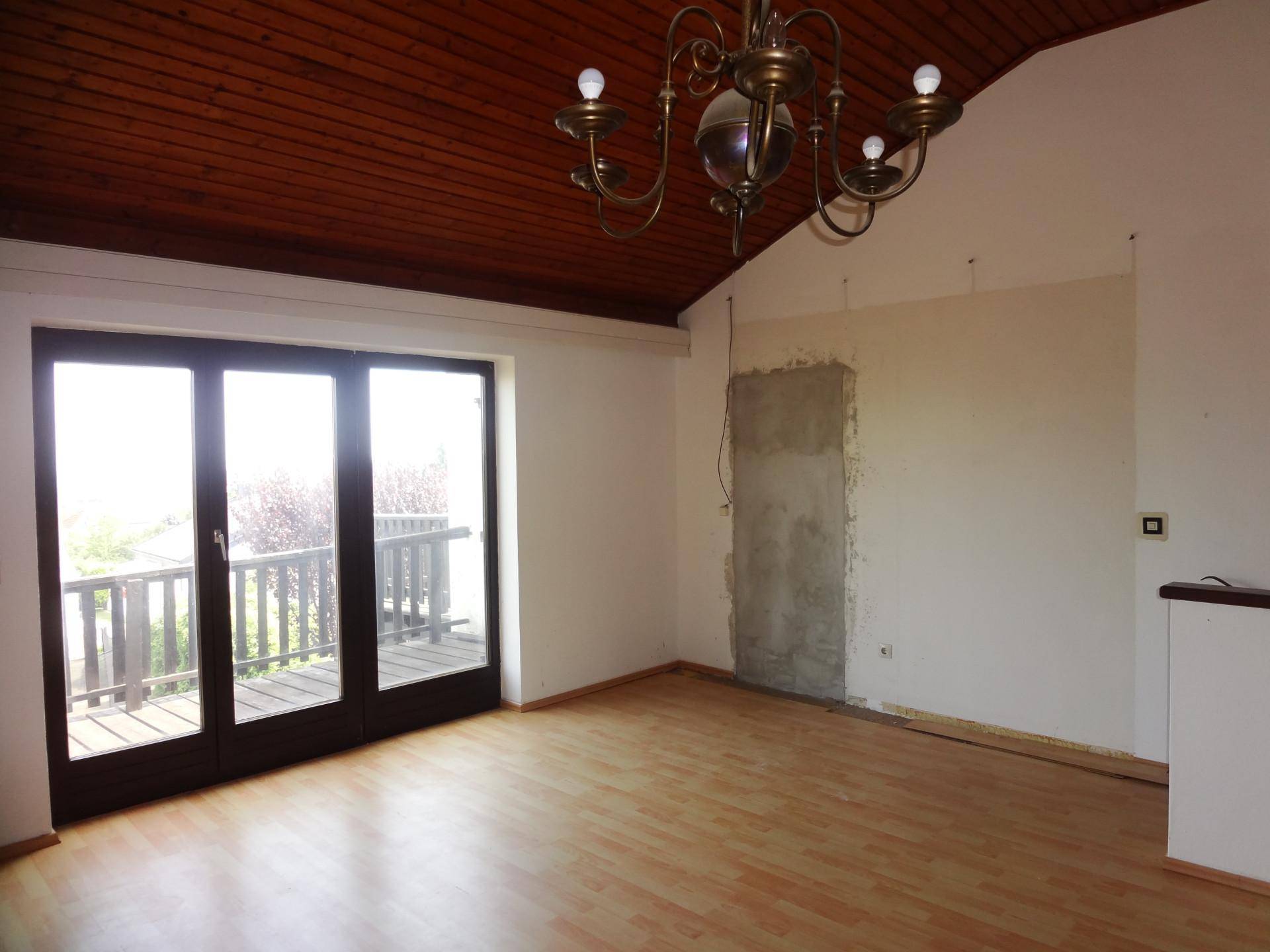 Geräumiger Wohnbereich mit Holzdachschräge, Laminatboden und Zugang zu einem Balkon.