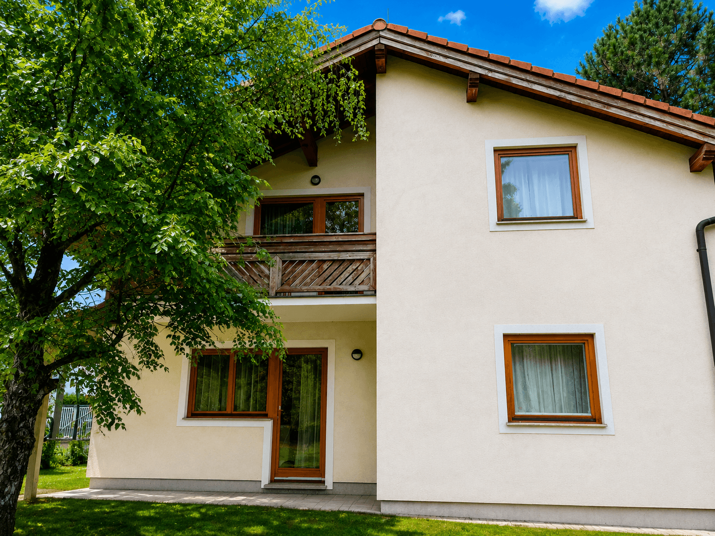 Rückseite des Hauses mit einem Holzbalkon und Zugang zum Garten, umgeben von grüner Natur.
